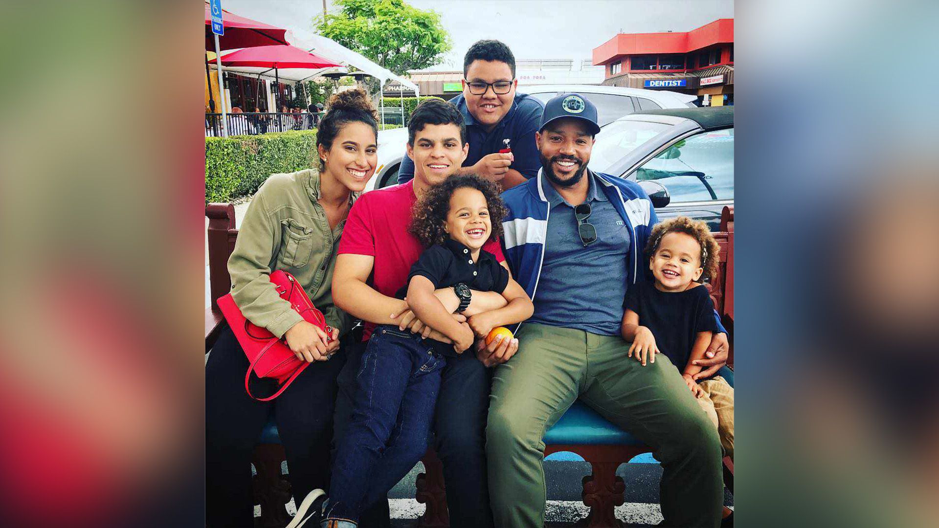 Donald Faison feliz sentado no jardim rodeado pelos seus filhos