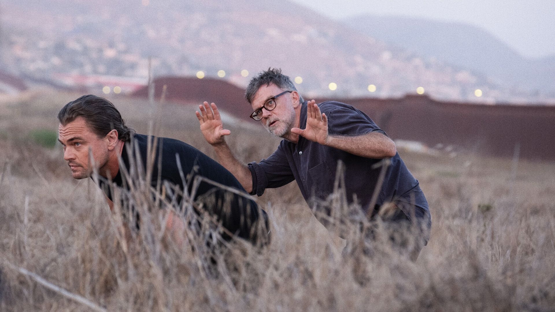 Paul Thomas Anderson e Leonardo DiCaprio caminhando agachados por entre capim alto