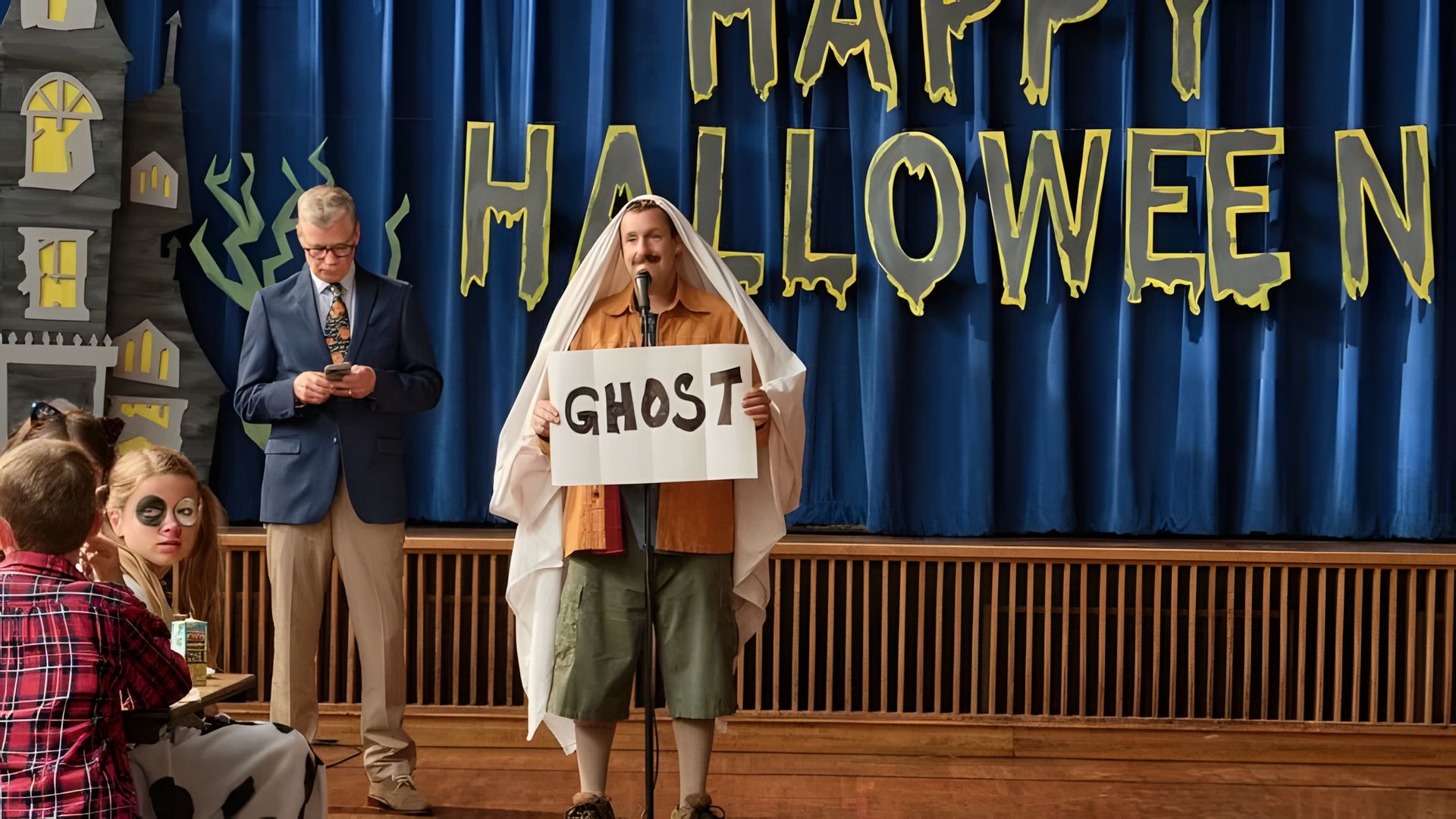 Adam Sandler com um lençol sobre a cabeça, segurando um cartaz que diz GHOST