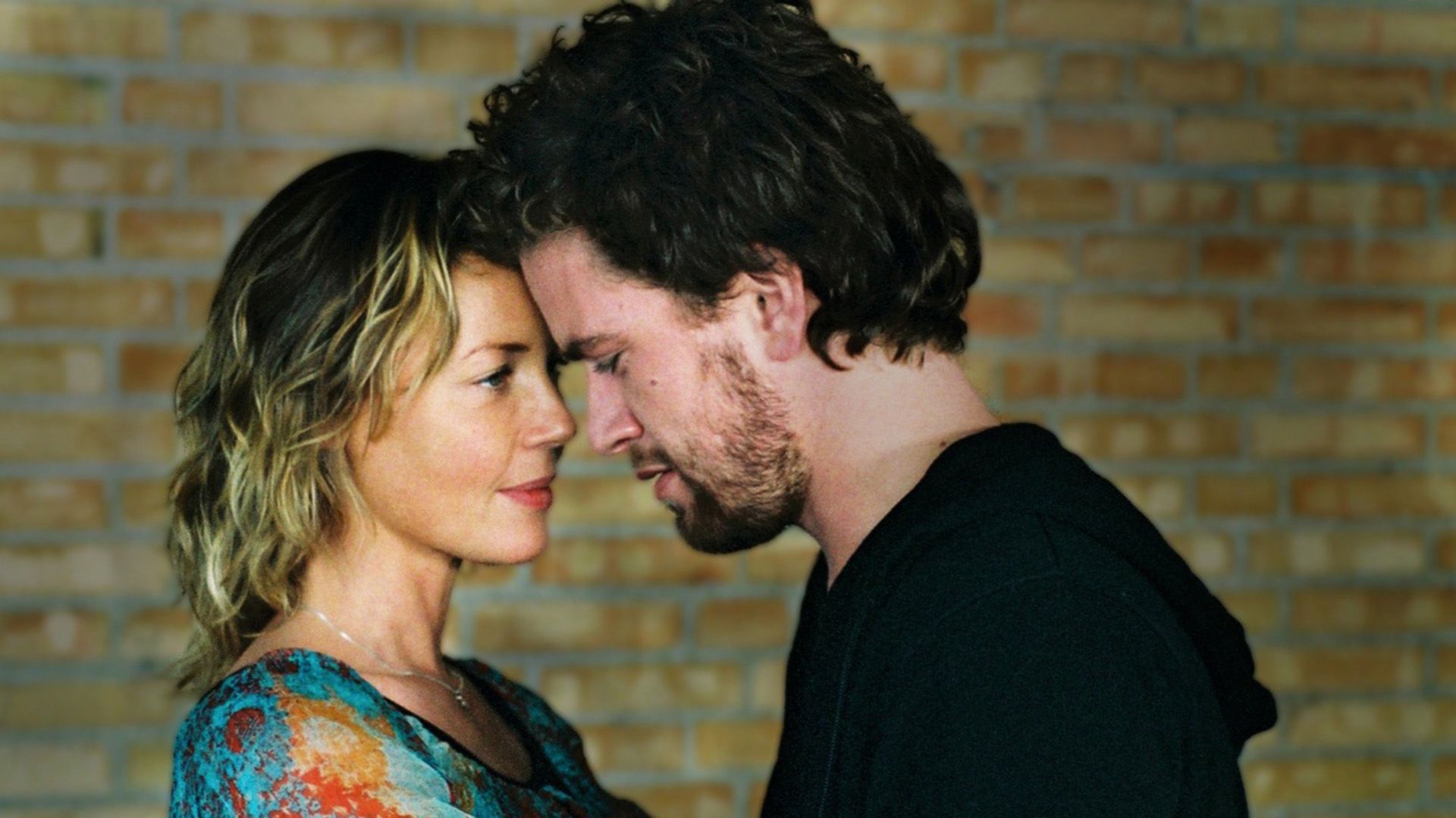Connie Nielsen e um homem de cabelo escuro encostam as testas um ao outro