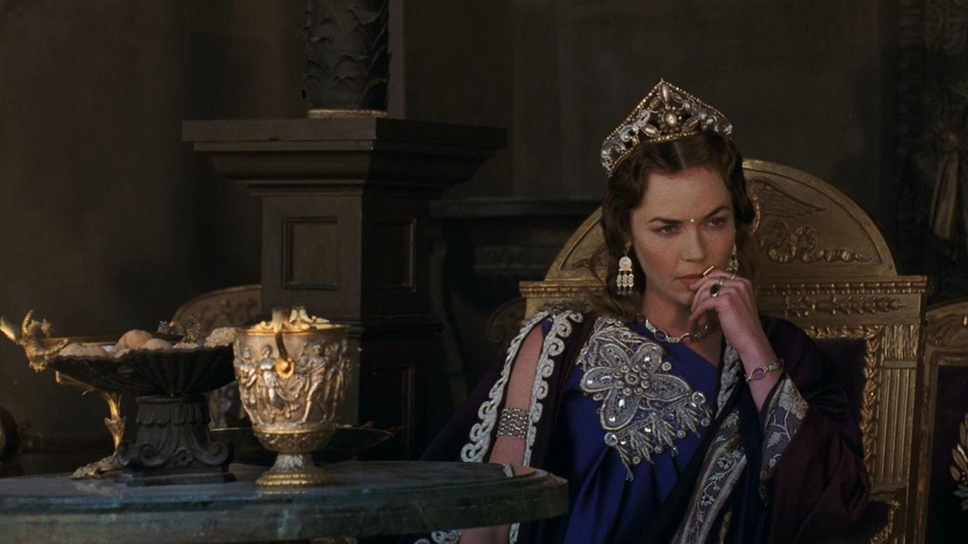 Connie Nielsen como Lucilla sentada pensativa num trono dourado