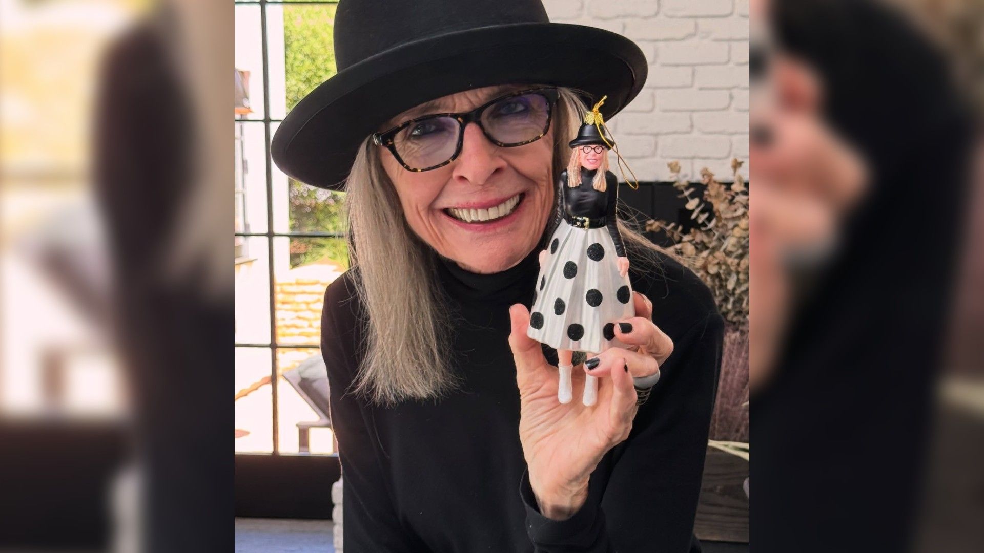 Diane Keaton, de chapéu, a mostrar um enfeite de Natal que é uma réplica exata dela