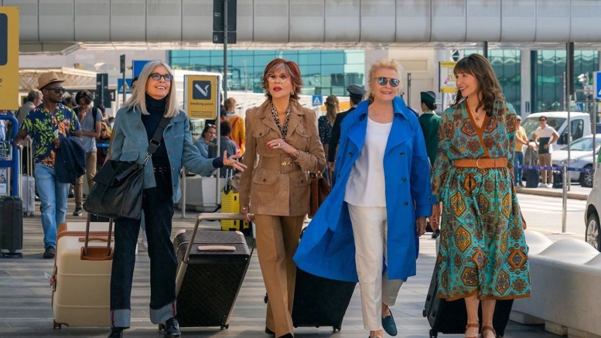 Quatro mulheres elegantemente vestidas a caminhar pelo aeroporto com as suas malas