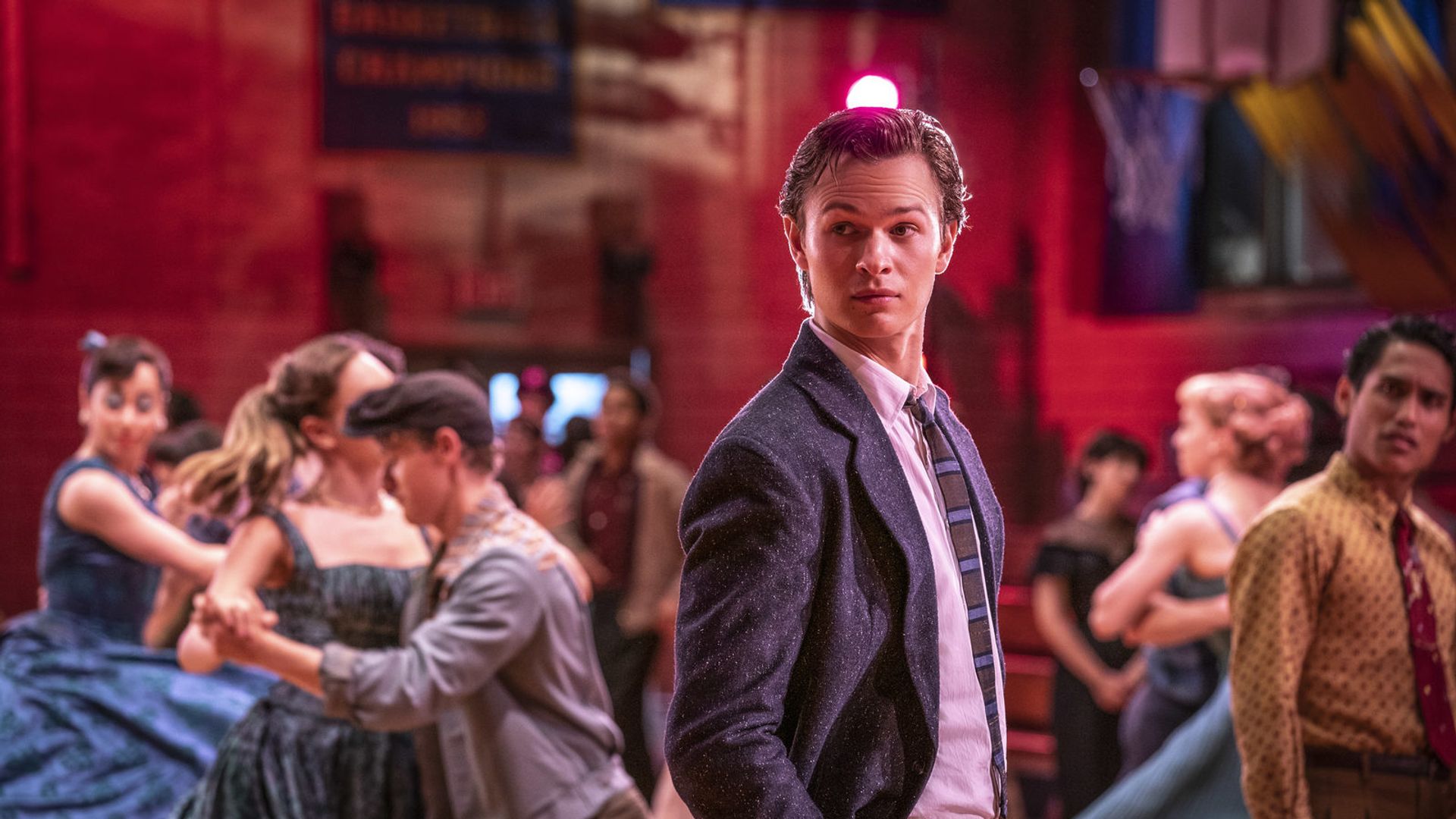 Ansel Elgort de fato e gravata num baile escolar com casais a rodopiar à sua volta