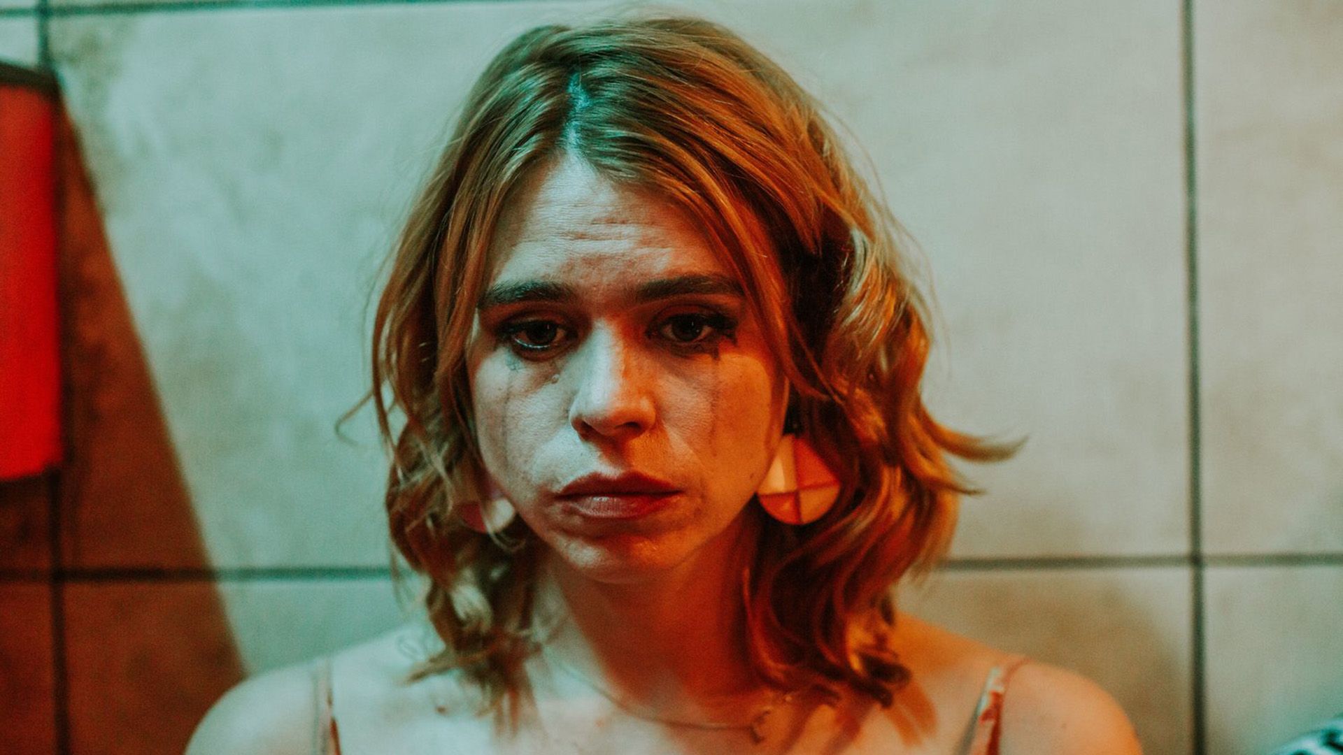 Uma Billie Piper triste com rímel borrado iluminada por luz vermelha