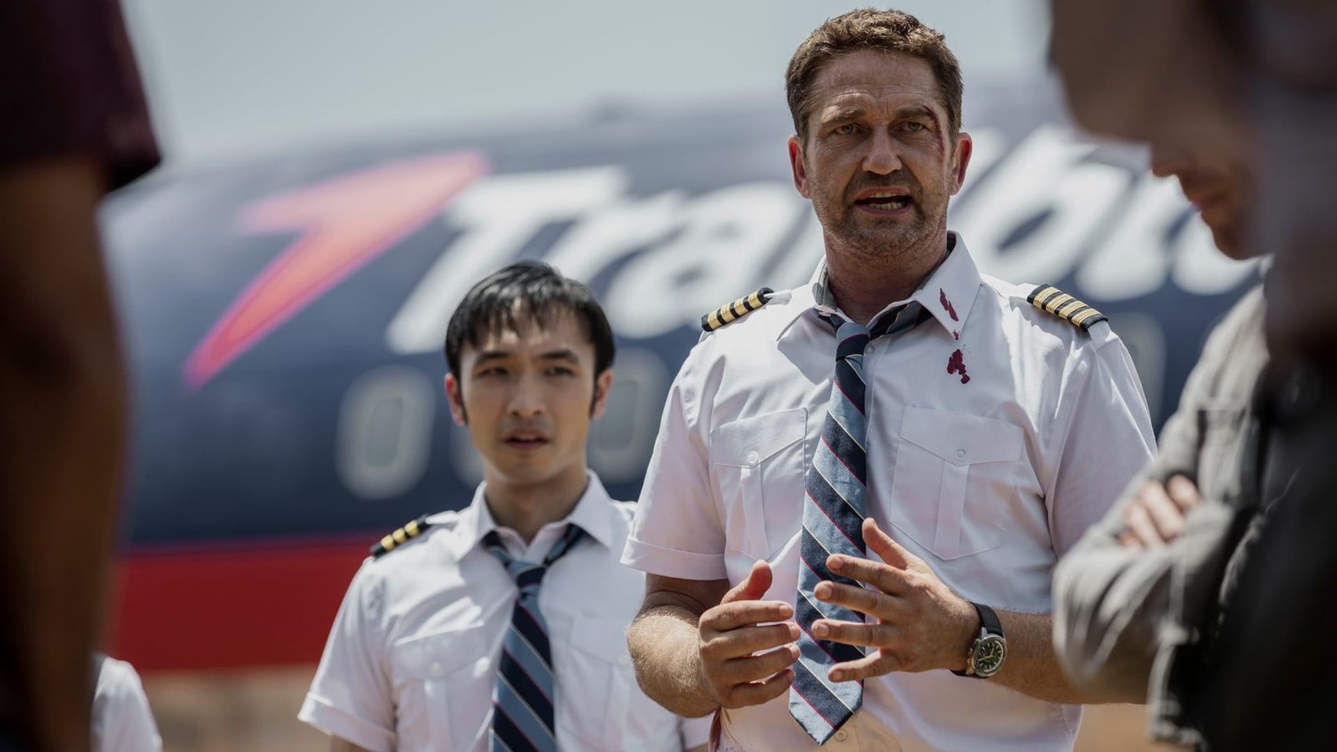 Gerard Butler em uniforme de piloto contra um cenário de avião, cena do filme