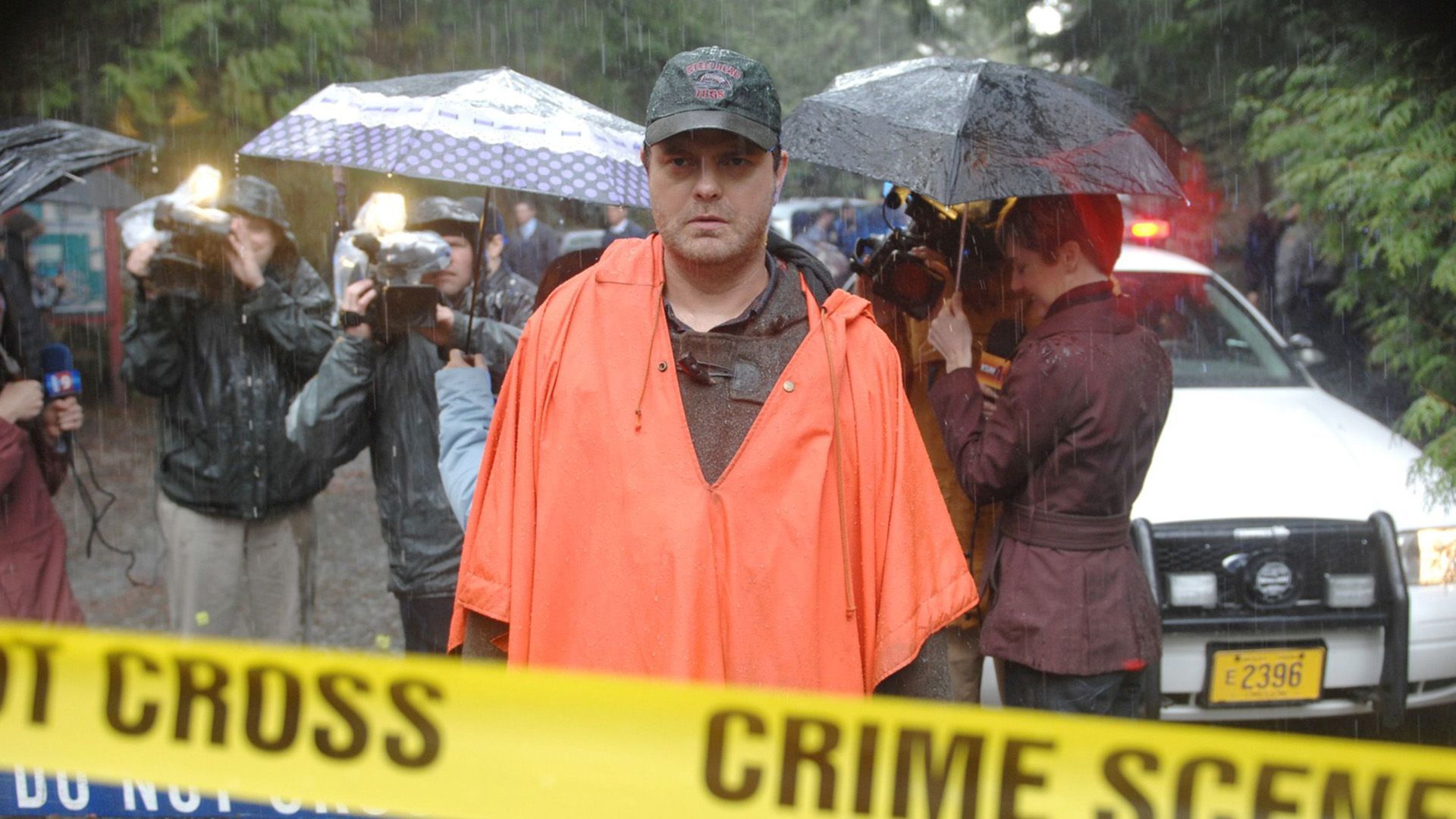Rainn Wilson com um casaco laranja à chuva atrás de fita policial amarela
