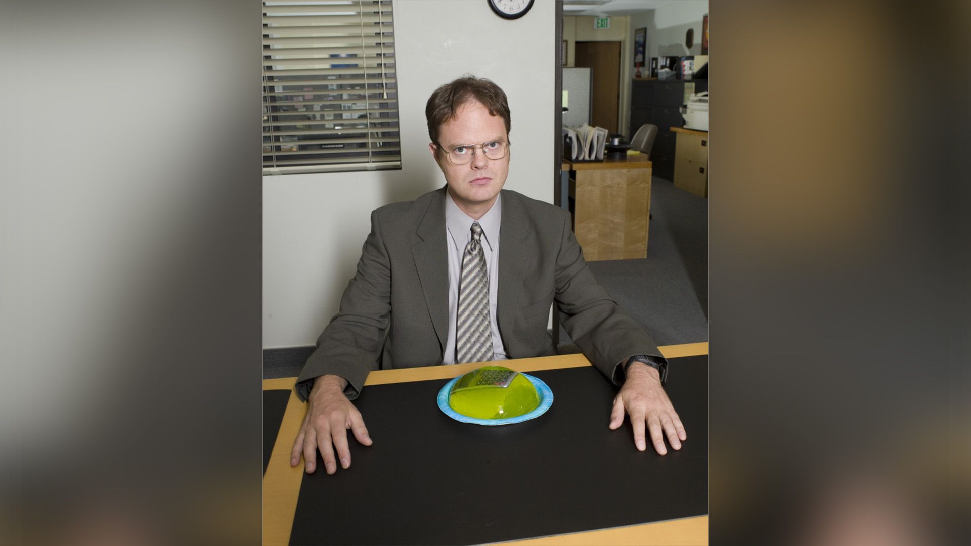 Rainn Wilson sentado a uma mesa com um prato à sua frente contendo uma calculadora coberta de gelatina verde