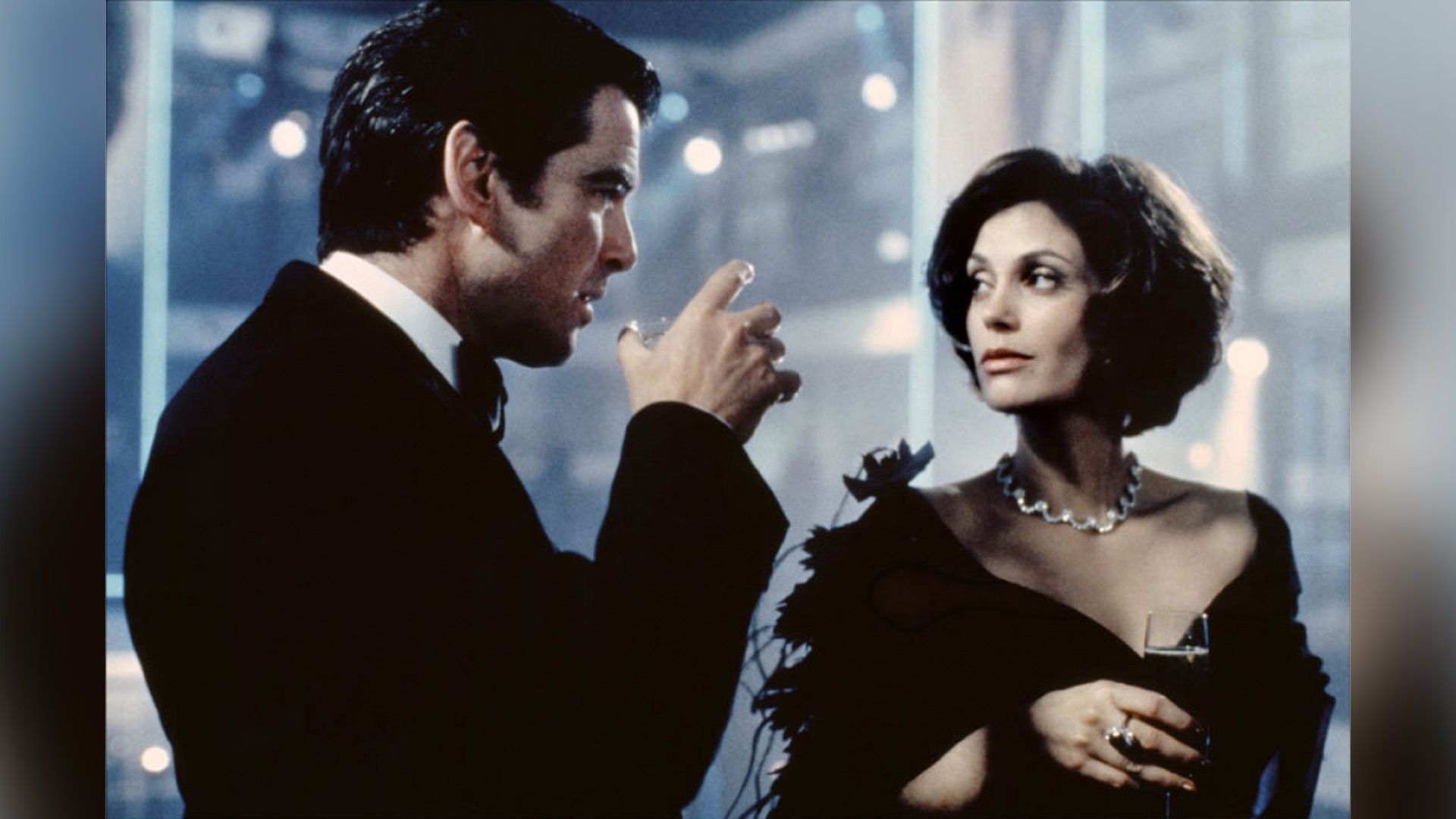Teri Hatcher num vestido de noite e colar de diamantes segura um copo com um homem de smoking ao seu lado