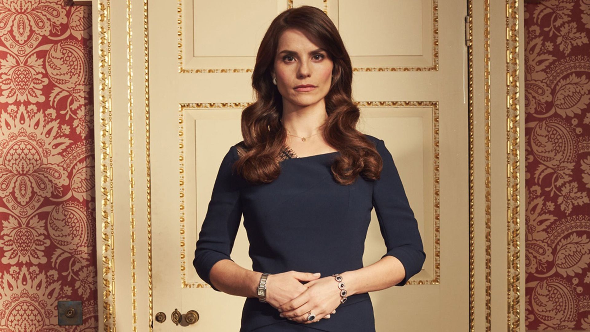 Charlotte Riley num vestido azul em frente a uma porta branca com acabamentos dourados