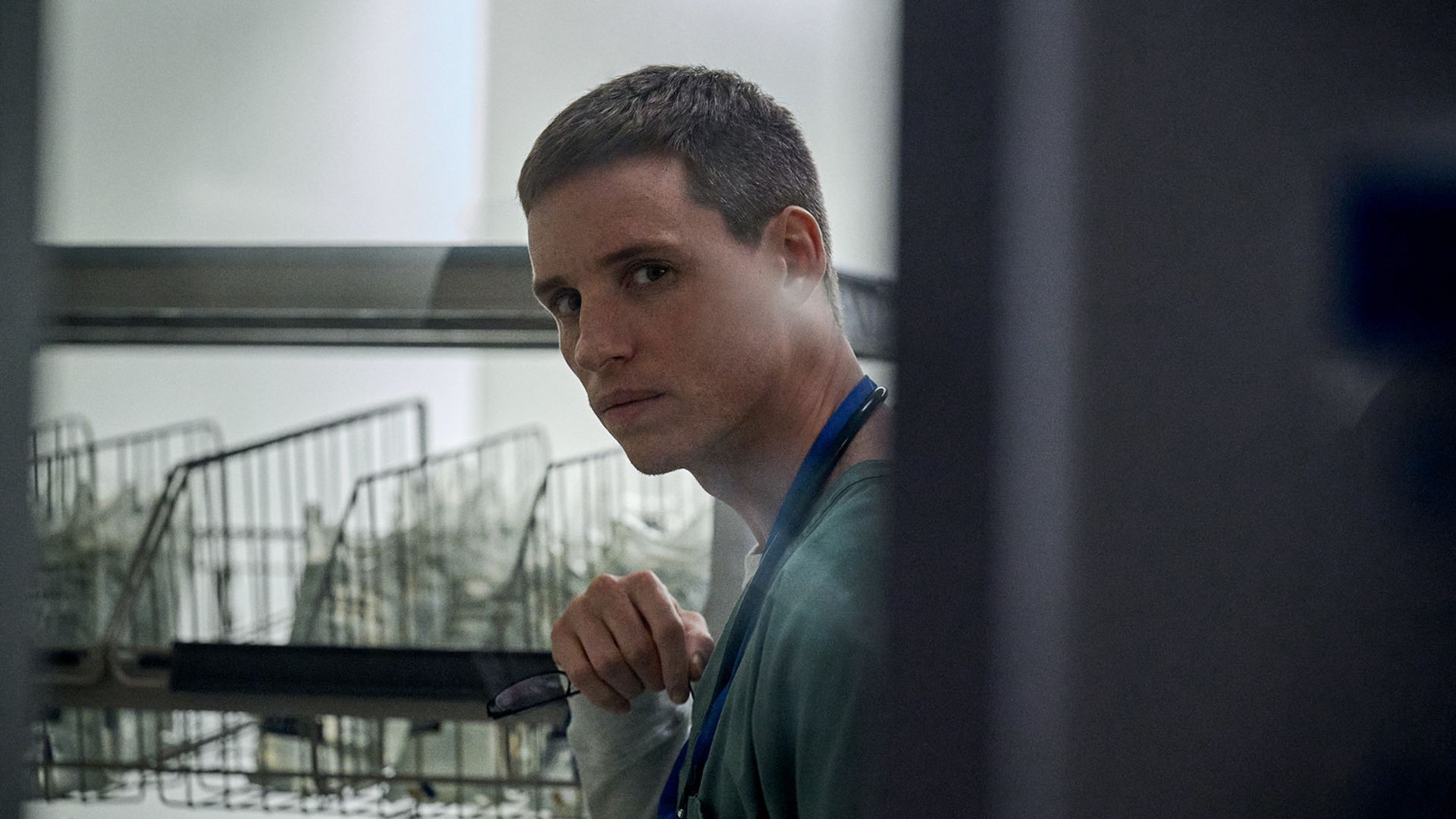Eddie Redmayne com cabelo curto espreita ao virar da esquina