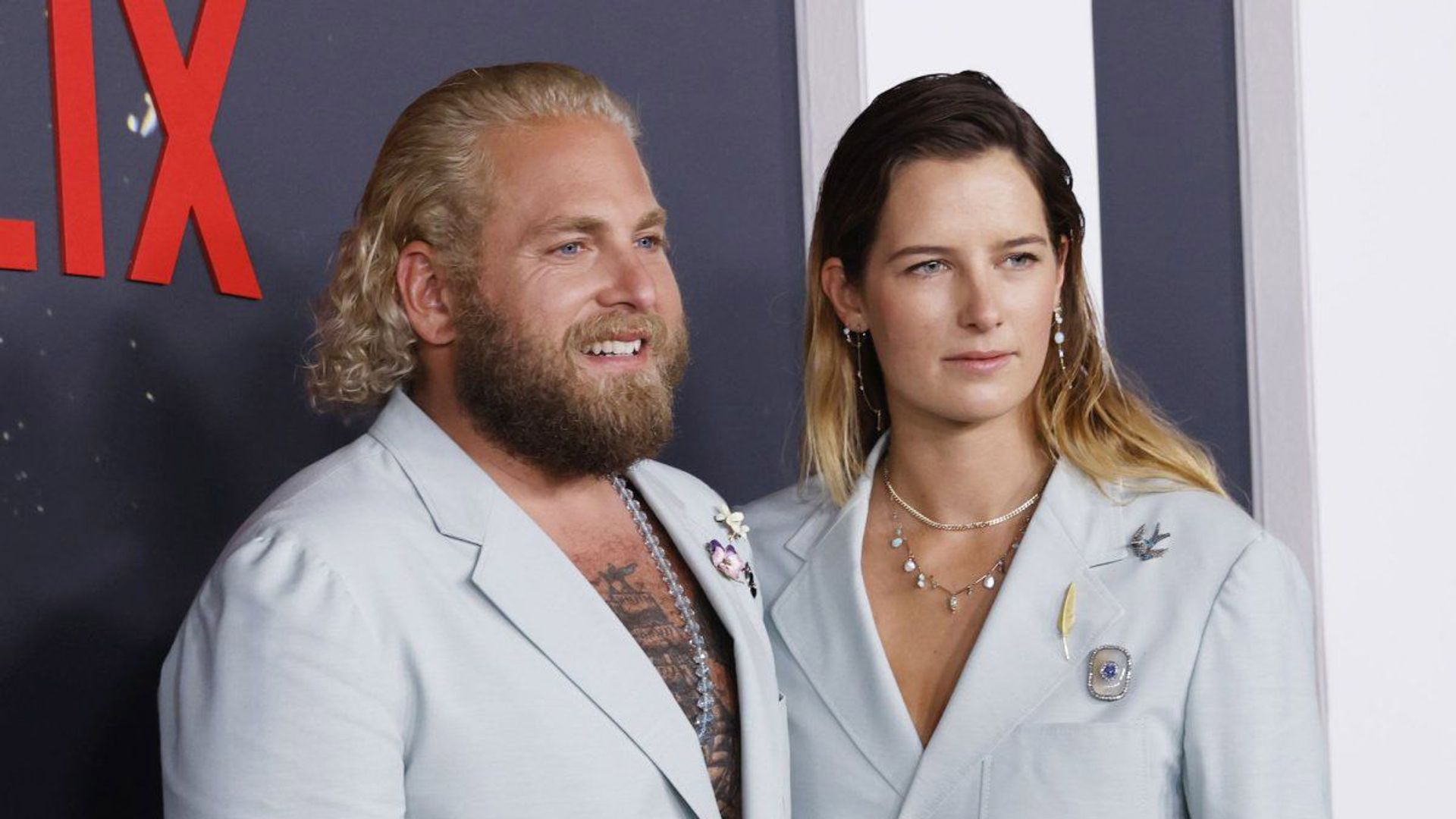 Jonah Hill e Sarah Brady posam em frente a um backdrop da Netflix