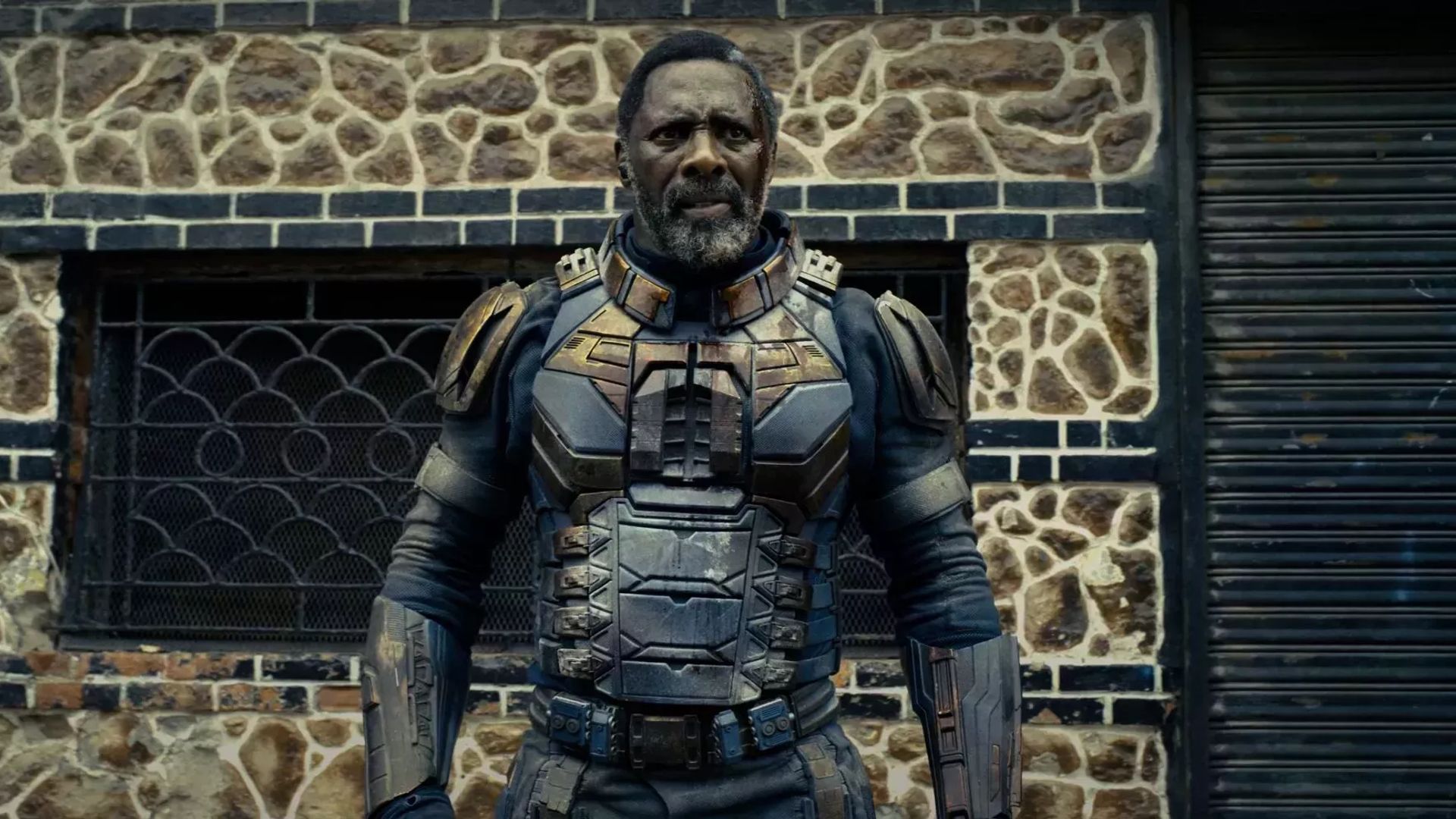 Idris Elba em armadura de super-herói contra um edifício de tijolos