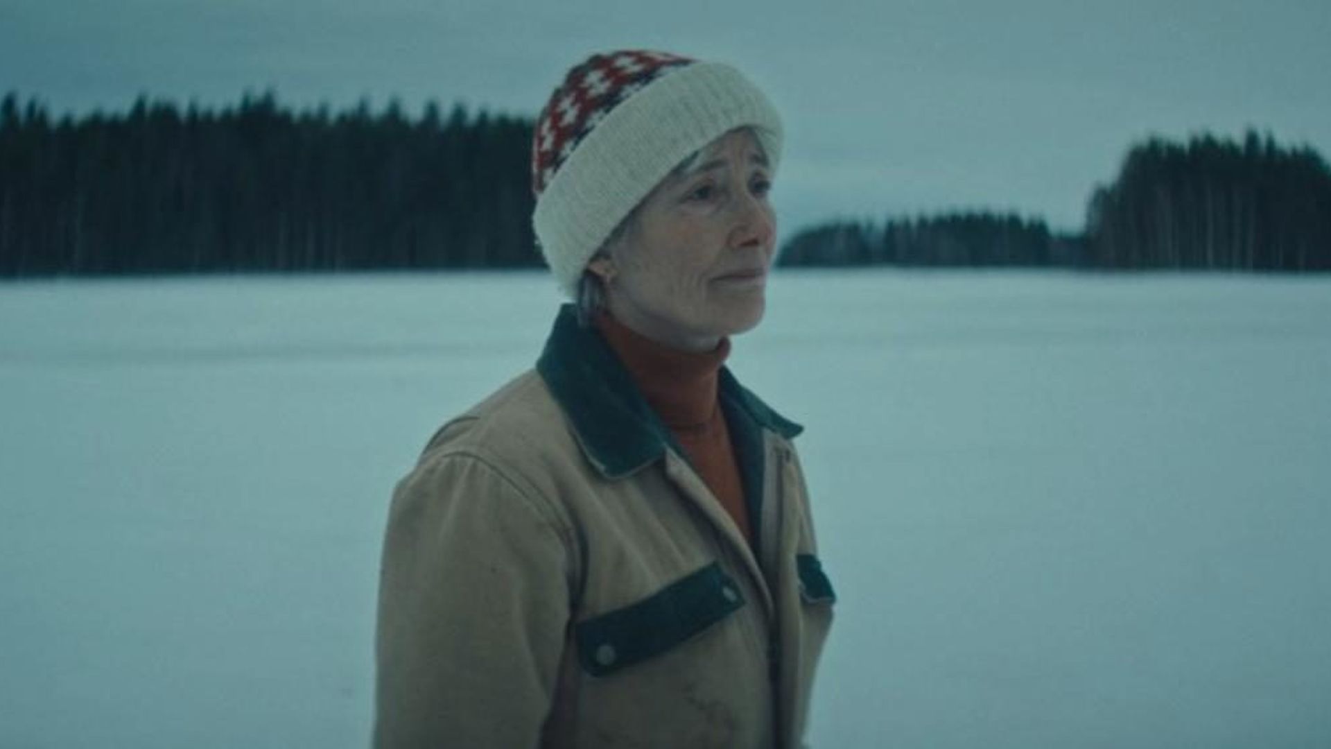 Emma Thompson com roupa de inverno contra um cenário nevado, fotografia com tonalidade azul
