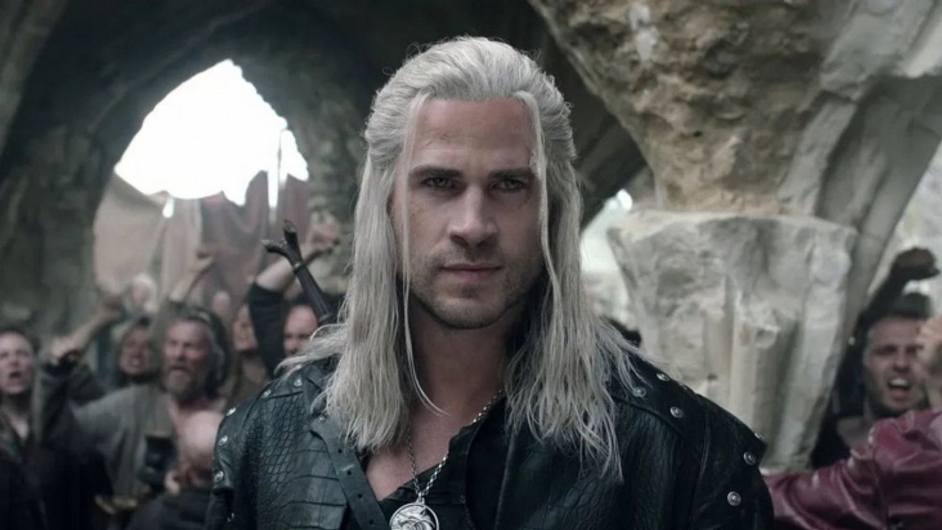 Liam Hemsworth caracterizado como Witcher: cabelo branco comprido, casaco de cabedal