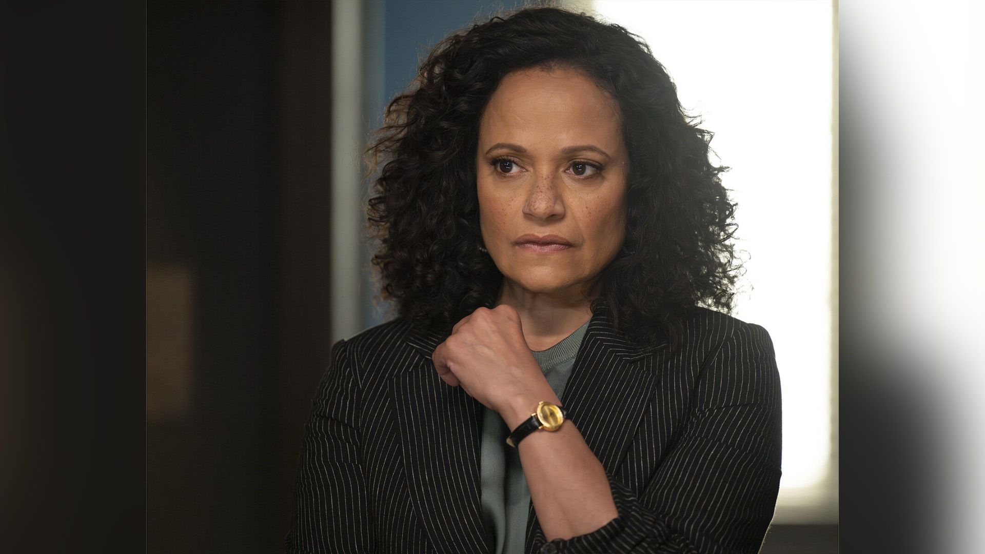 Judy Reyes com um blazer às riscas olha pensativamente para o lado