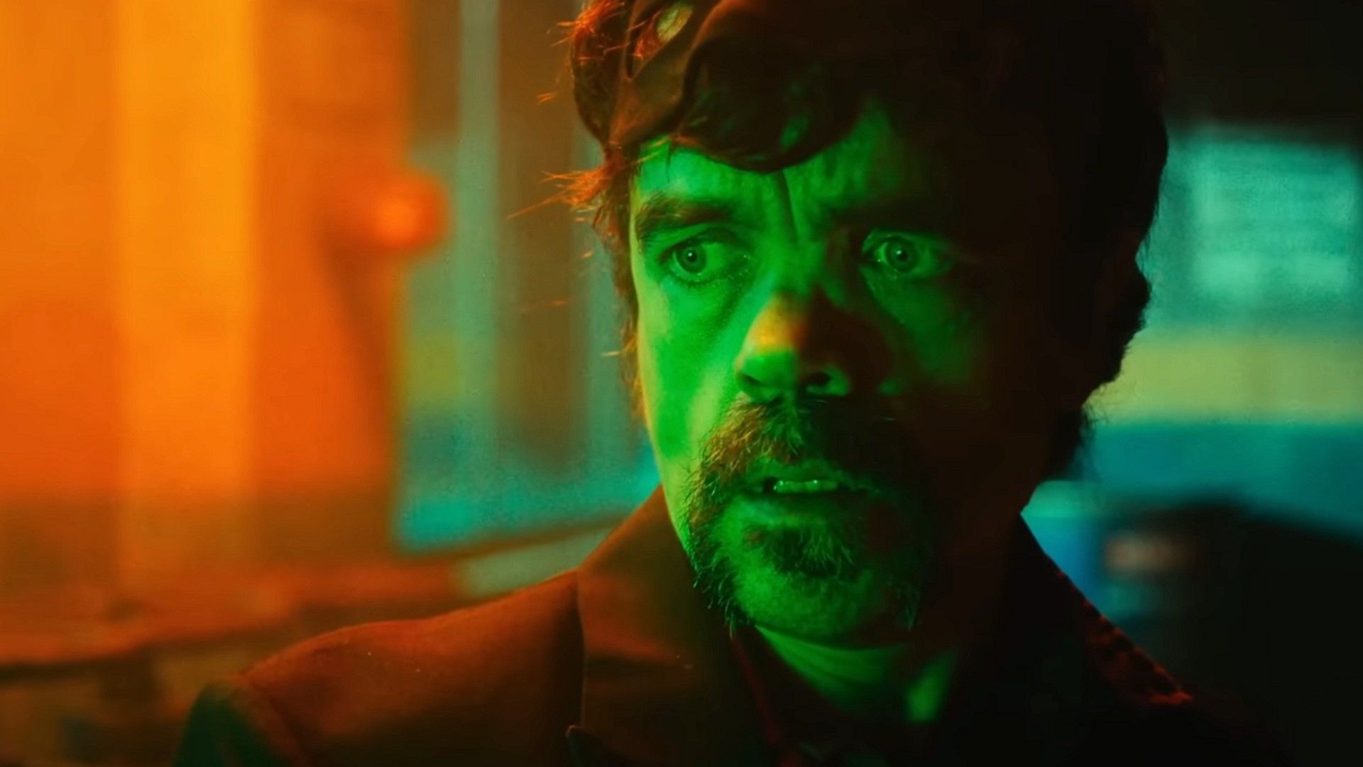 Peter Dinklage numa sala escura iluminada por luz verde e laranja