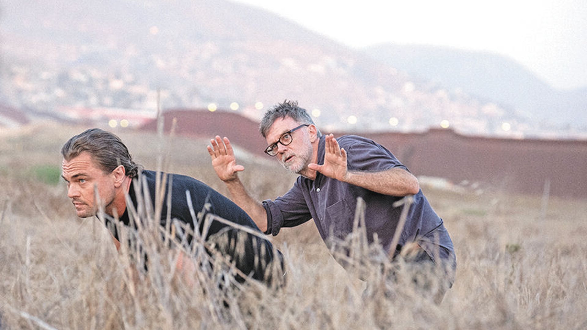 Leonardo DiCaprio e Paul Thomas Anderson a caminhar por um campo, escondidos na relva