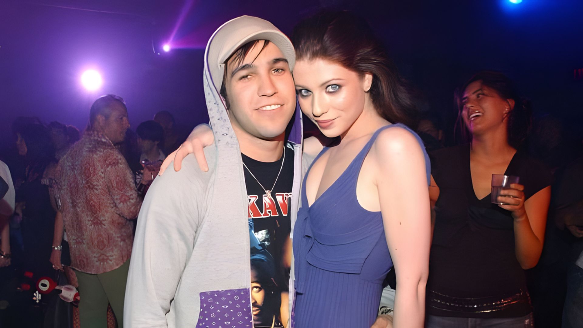 A atriz Michelle Trachtenberg e o músico Pete Wentz abraçam-se enquanto as pessoas se divertem em segundo plano