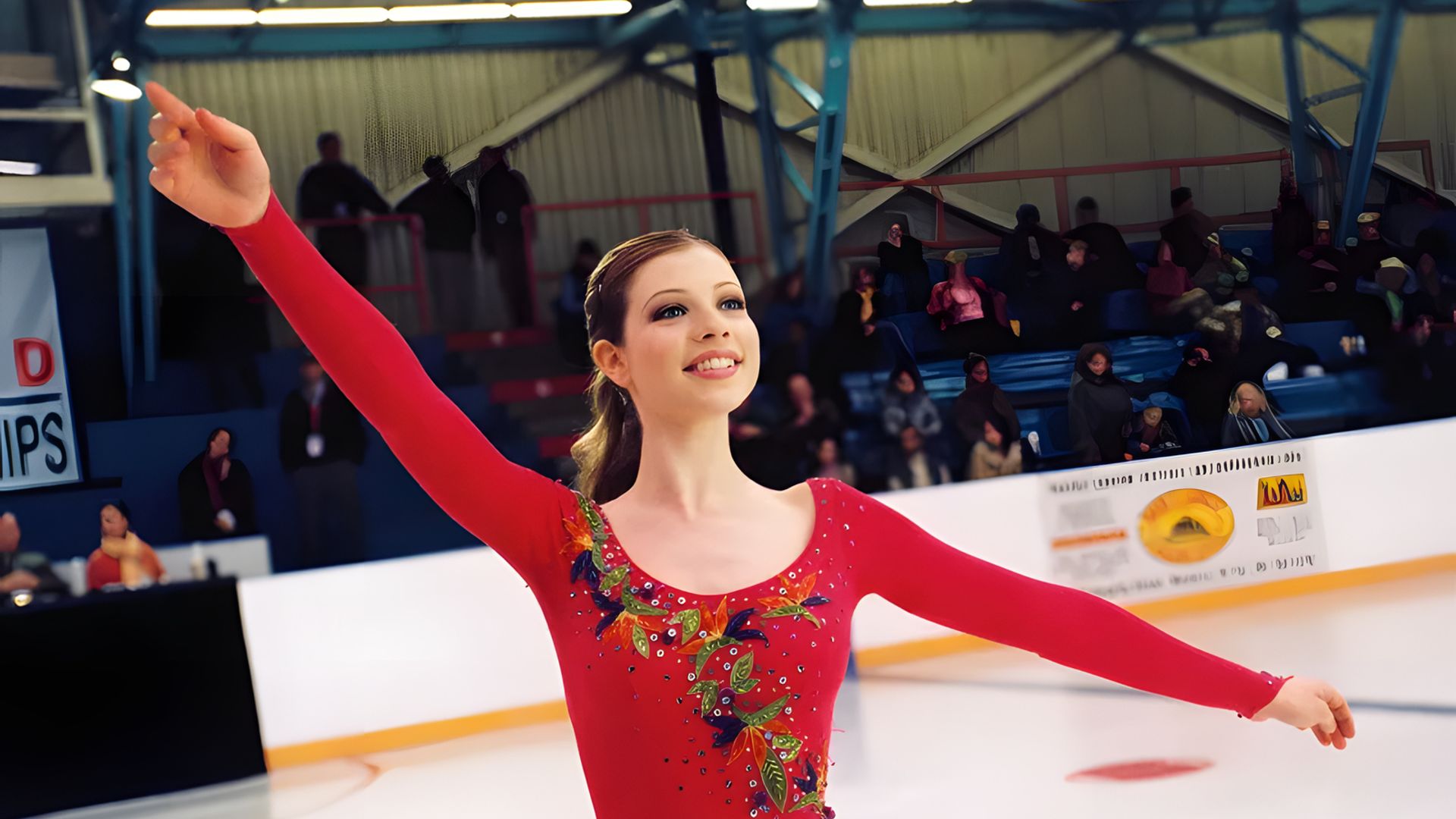 Michelle Trachtenberg num fato de patinadora vermelho dança no gelo, com os braços erguidos