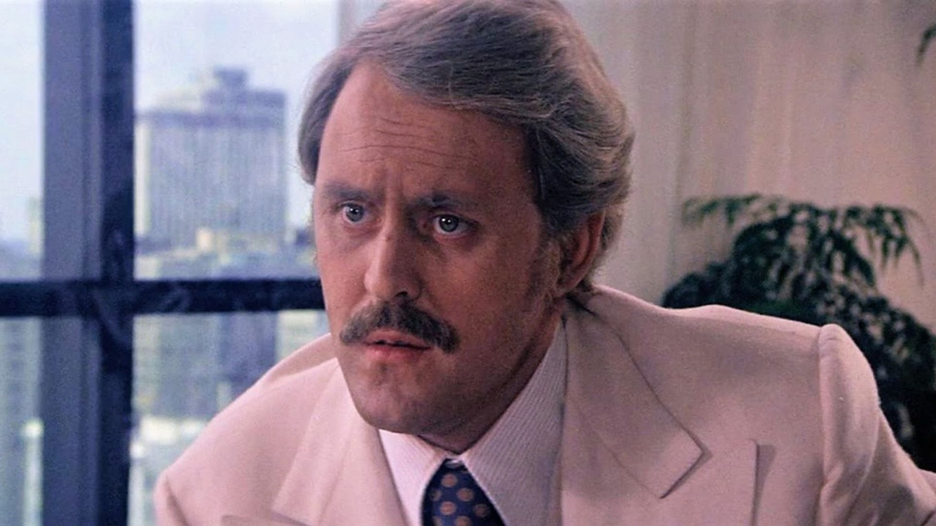 John Lithgow com bigode e casaco creme numa cena do filme "Obsession"