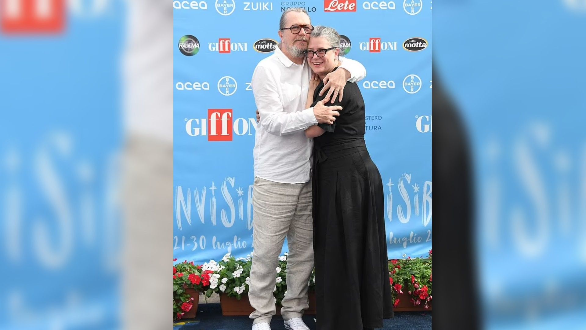 Gary Oldman e Gisele Schmidt abraçados e sorrindo contra um banner azul com logótipos de Giffoni