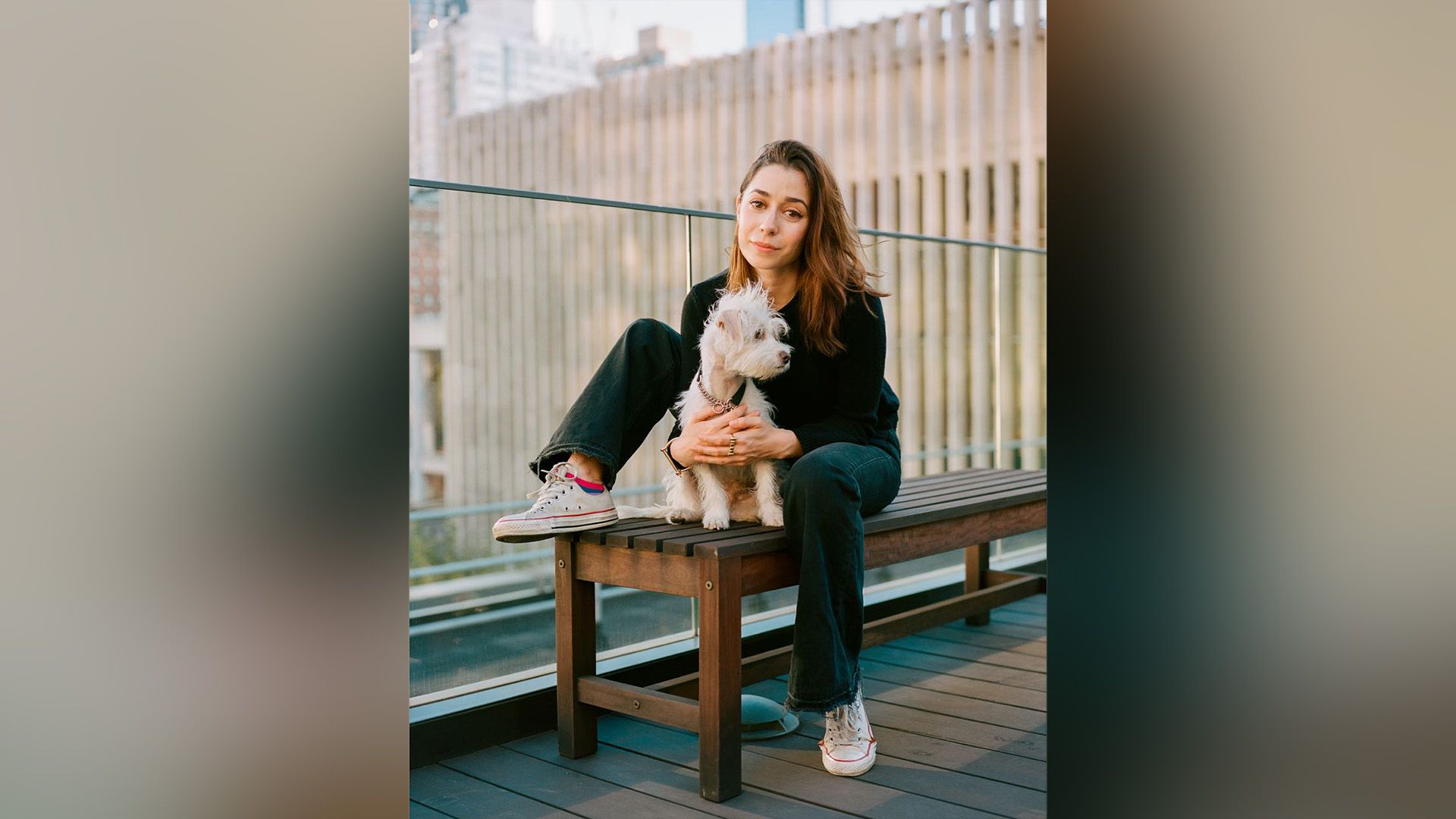 Cristin Milioti sentada num banco, abraçando um pequeno cão branco e fofo