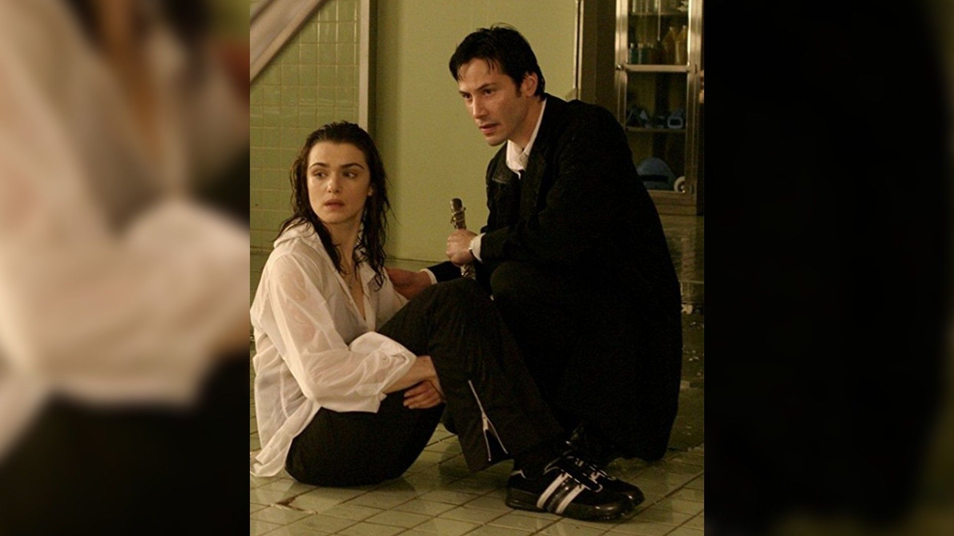 Rachel Weisz e Keanu Reeves sentados no chão um ao lado do outro