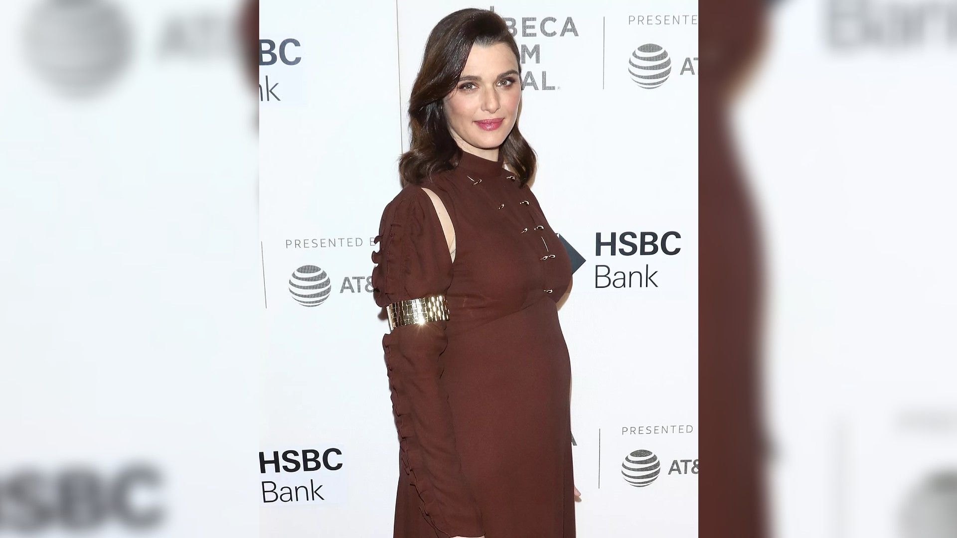 Rachel Weisz num vestido bordeaux de corpo inteiro, mostrando claramente que está à espera de um filho