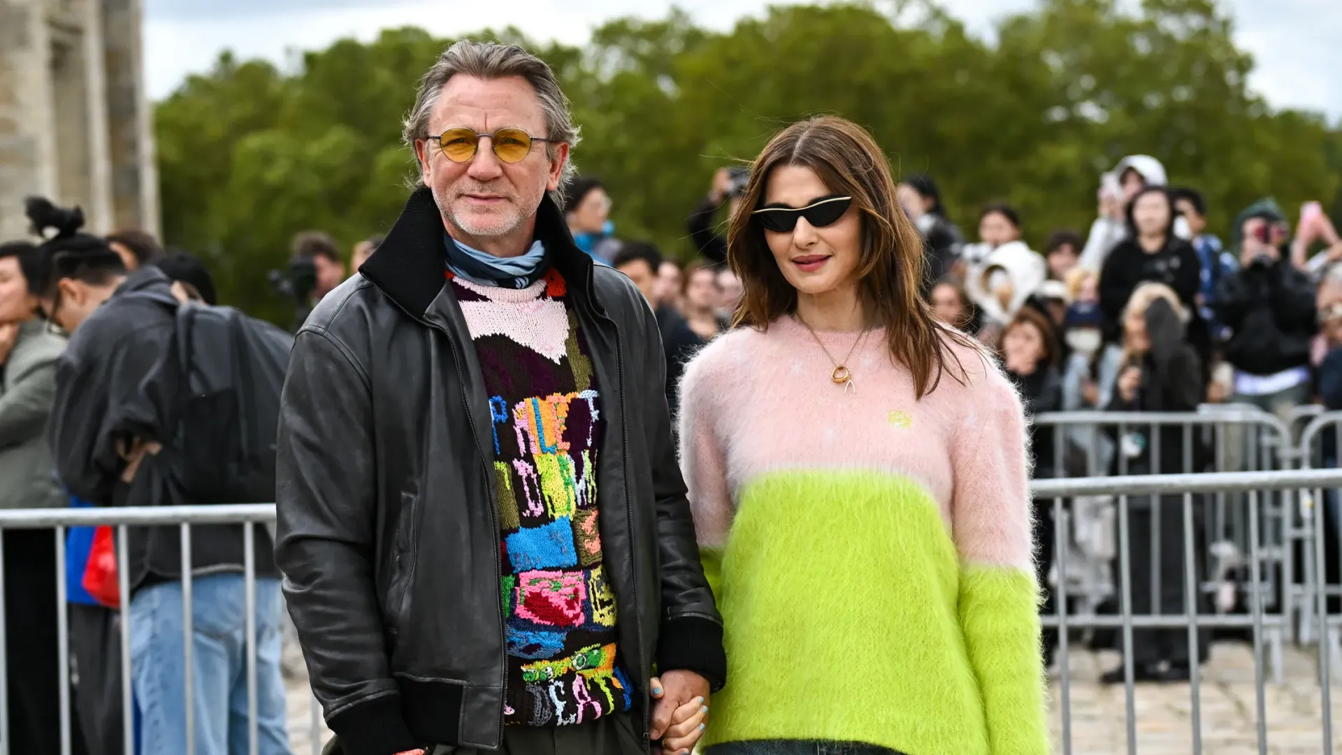 Rachel Weisz numa camisola branca e verde e Daniel Craig num casaco de cabedal preto e camisola colorida de mãos dadas