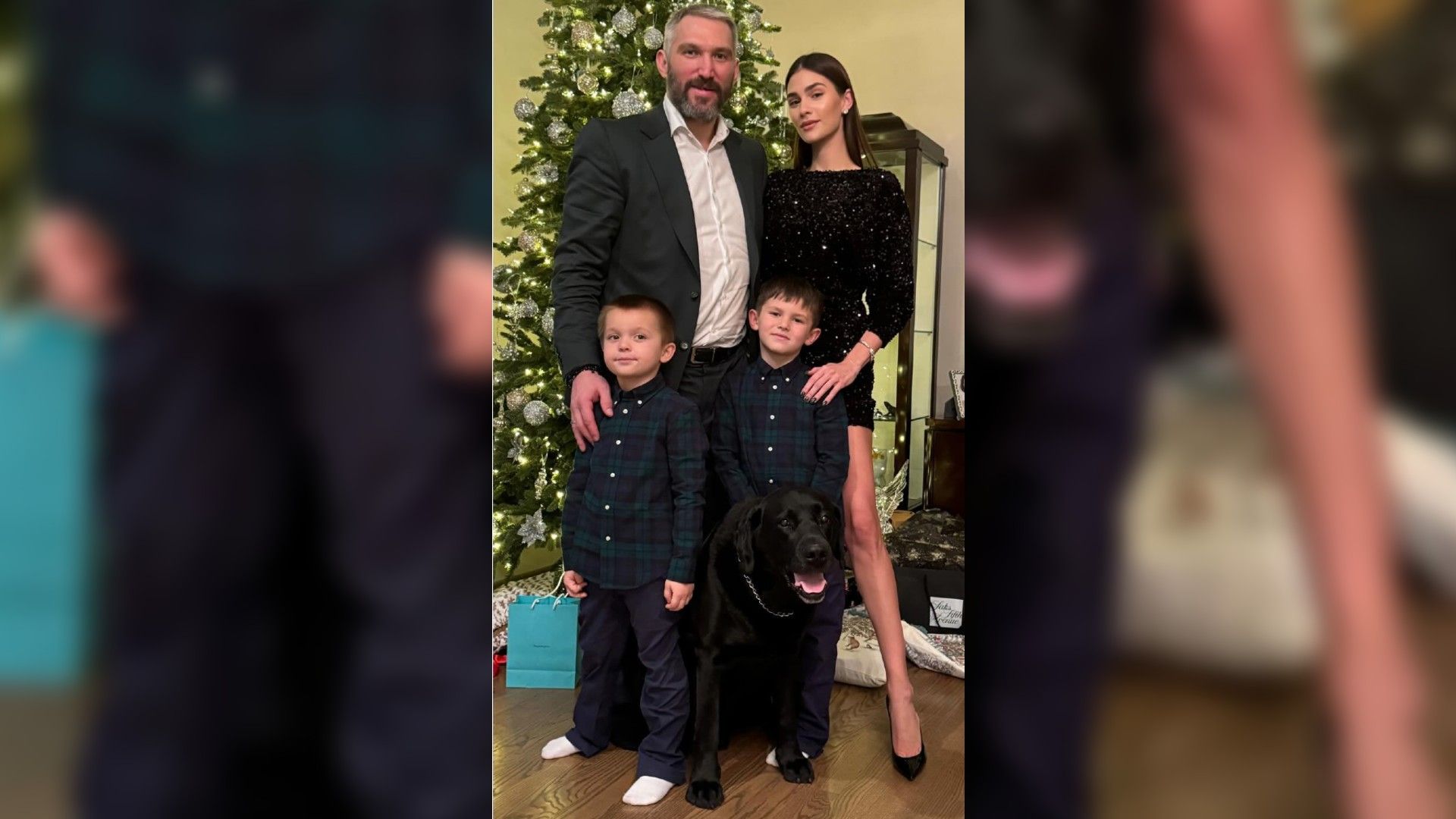 Alexander Ovechkin e Anastasia Shubskaya com dois rapazes e um cão preto posam junto à árvore de Ano Novo, os pais estão vestidos festivamente