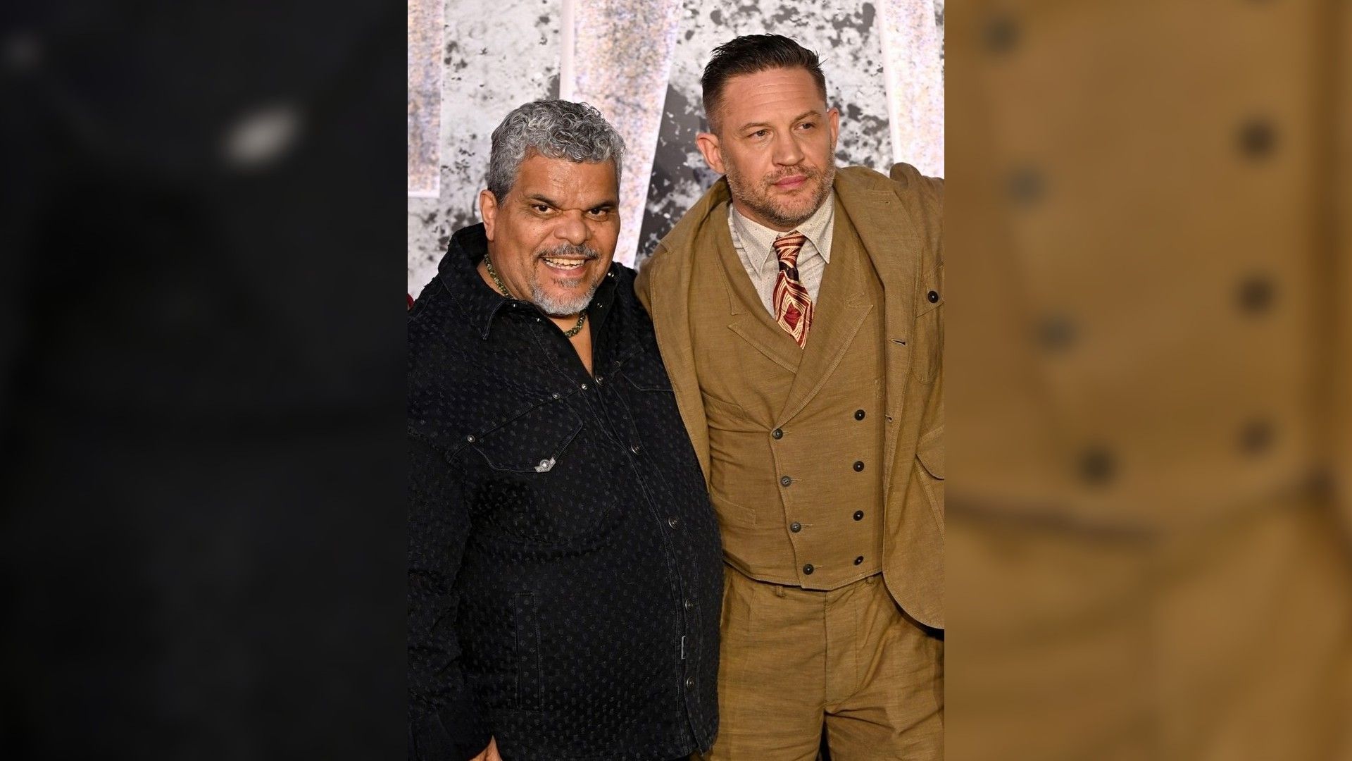 Luis Guzmán e Tom Hardy posam na passadeira vermelha: um numa camisa escura, o outro num fato castanho com gravata