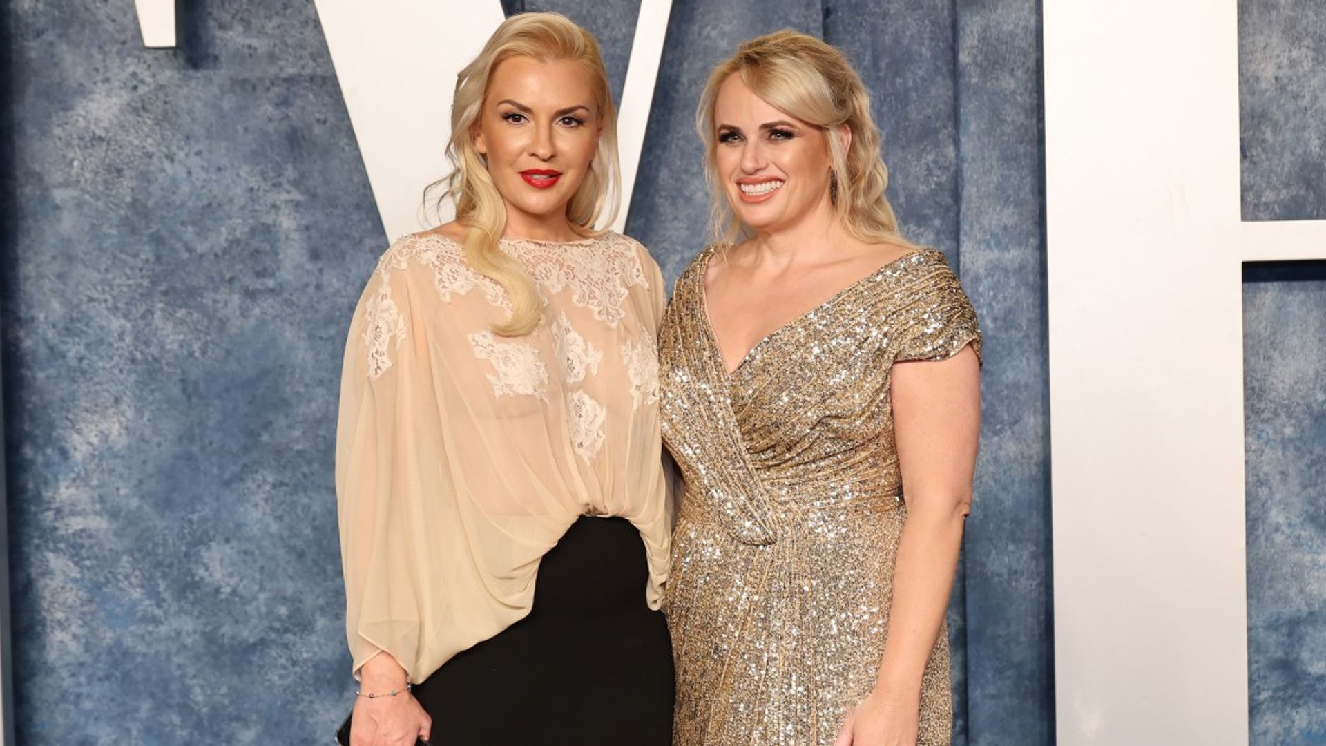 Rebel Wilson e Ramona Agruma de pé em vestidos contra um fundo claro
