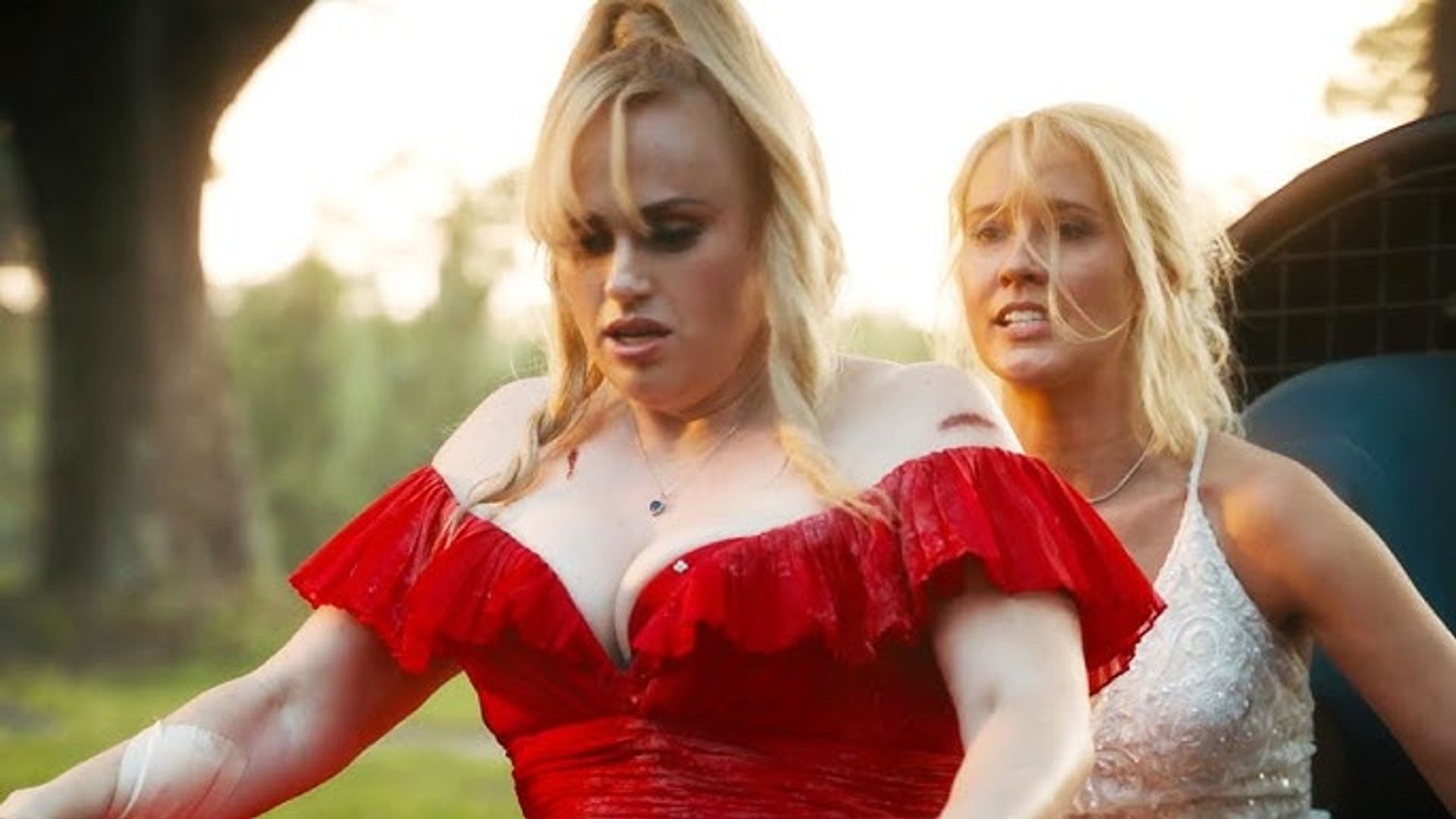 Rebel Wilson num vestido vermelho e Anna Camp de branco a andar de bicicleta