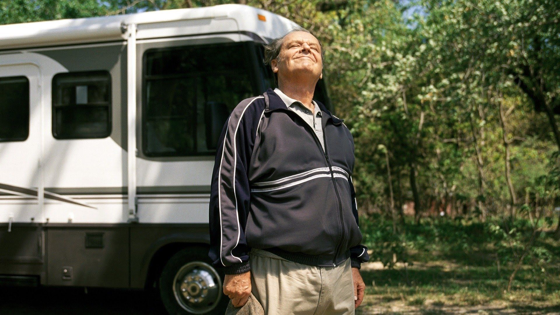 Jack Nicholson em fato de treino está em frente a uma autocaravana e aproveita um dia ensolarado rodeado de árvores