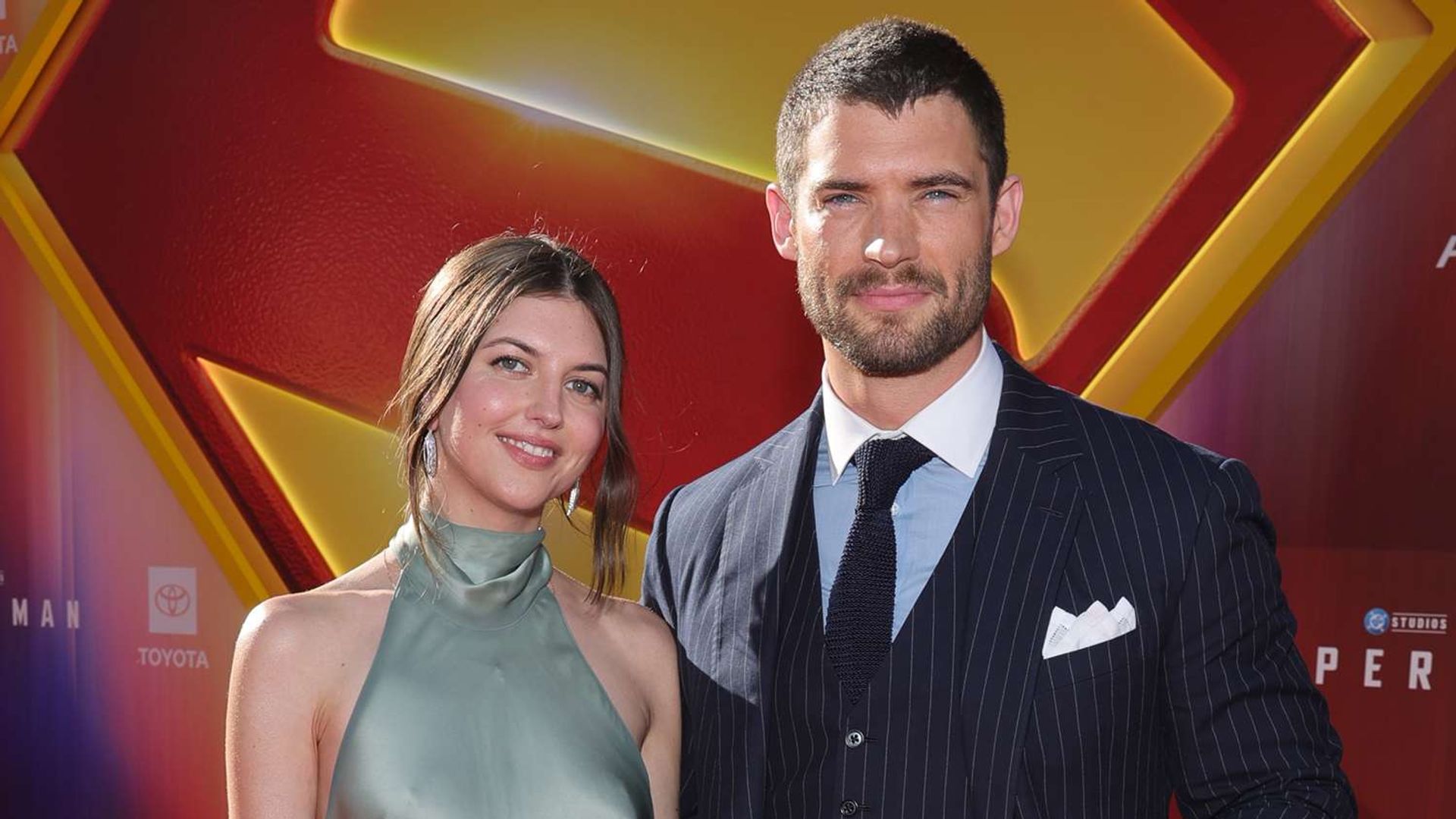 David Corenswet e Julia Warner posam contra o cenário fotográfico