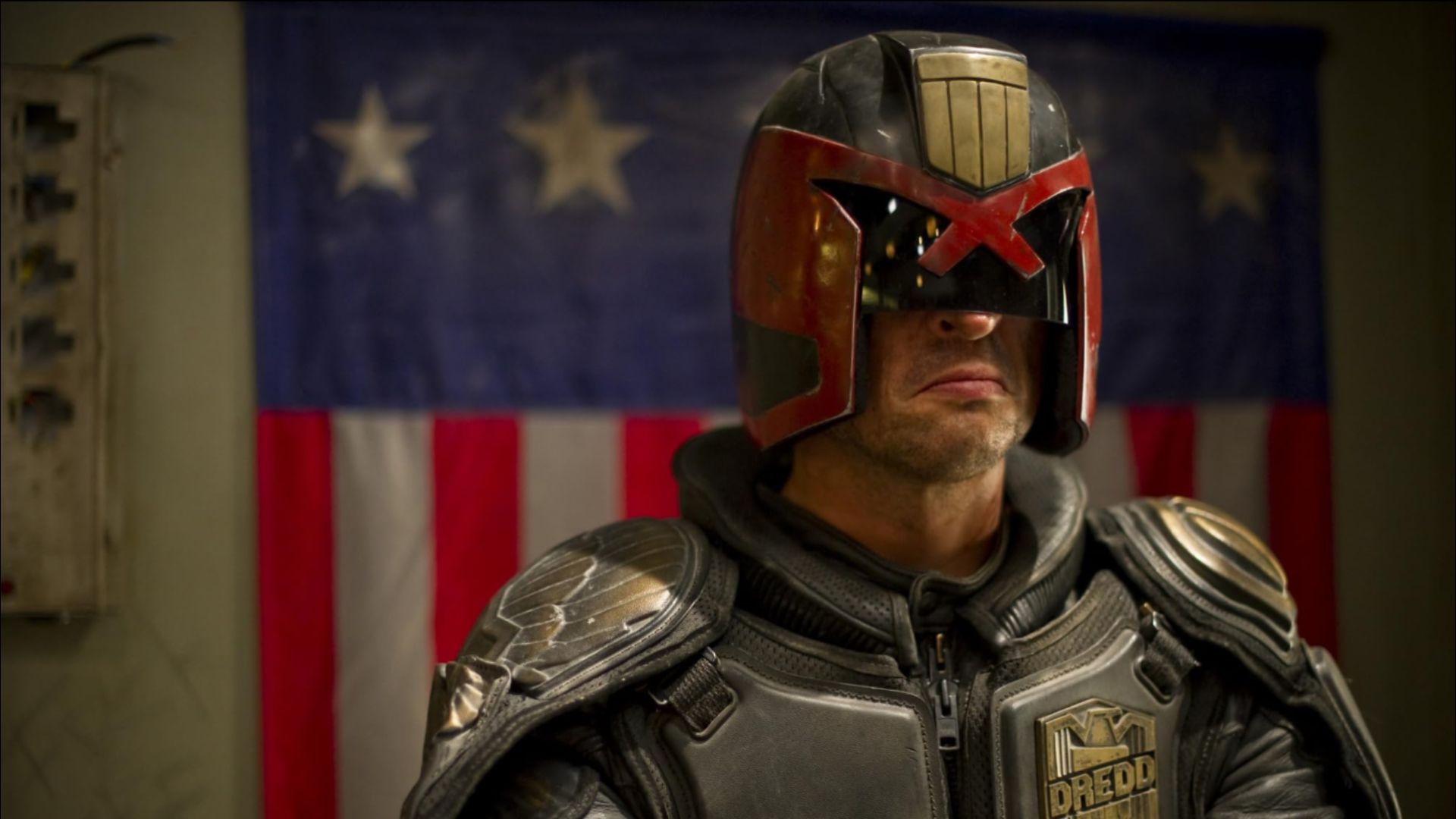 Ator Karl Urban num fato futurista cinzento e capacete preto-vermelho