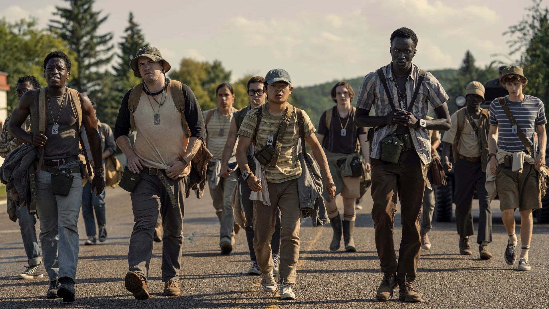 Um grupo de jovens com roupas de caminhada a caminhar ao longo de uma estrada num dia de verão, com árvores e colinas ao fundo
