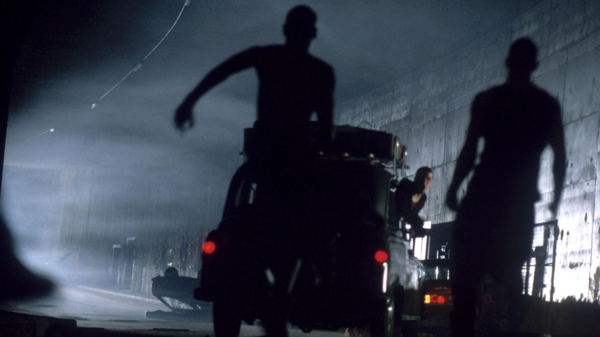 O ator Cillian Murphy junto a um carro enquanto zombies correm na sua direção
