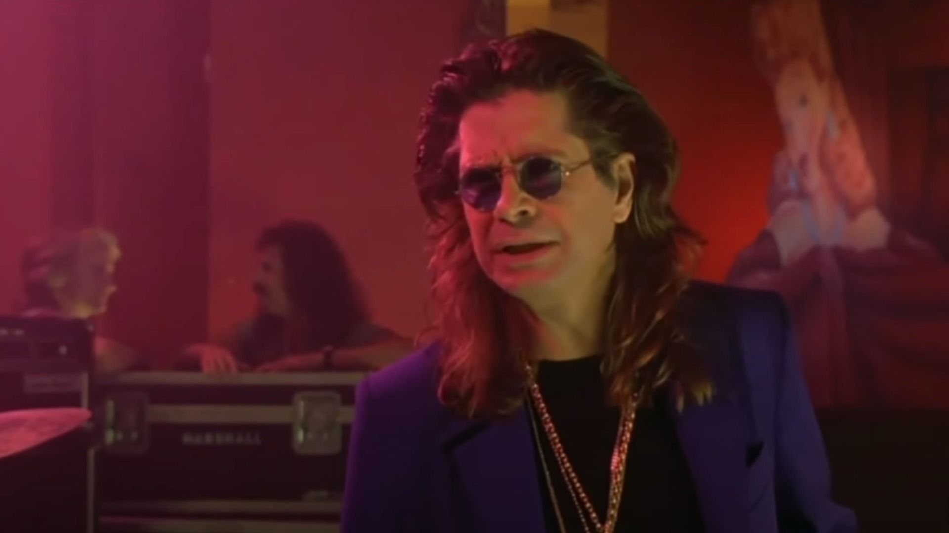 O cantor Ozzy Osbourne num blazer azul e corrente dourada em pé no palco