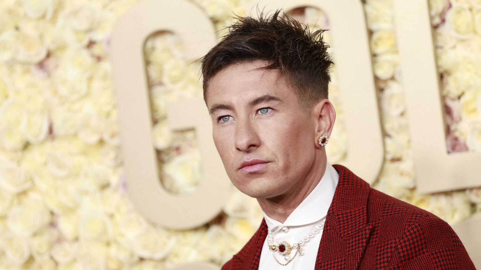 Ator Barry Keoghan num casaco vermelho com um brinco contra um fundo amarelo
