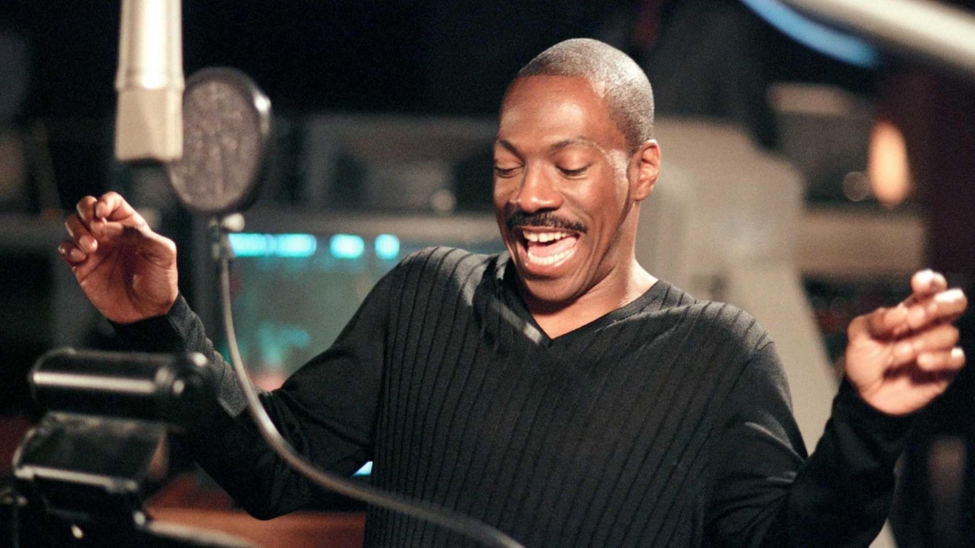 O ator Eddie Murphy numa camisola preta está ao microfone e sorri