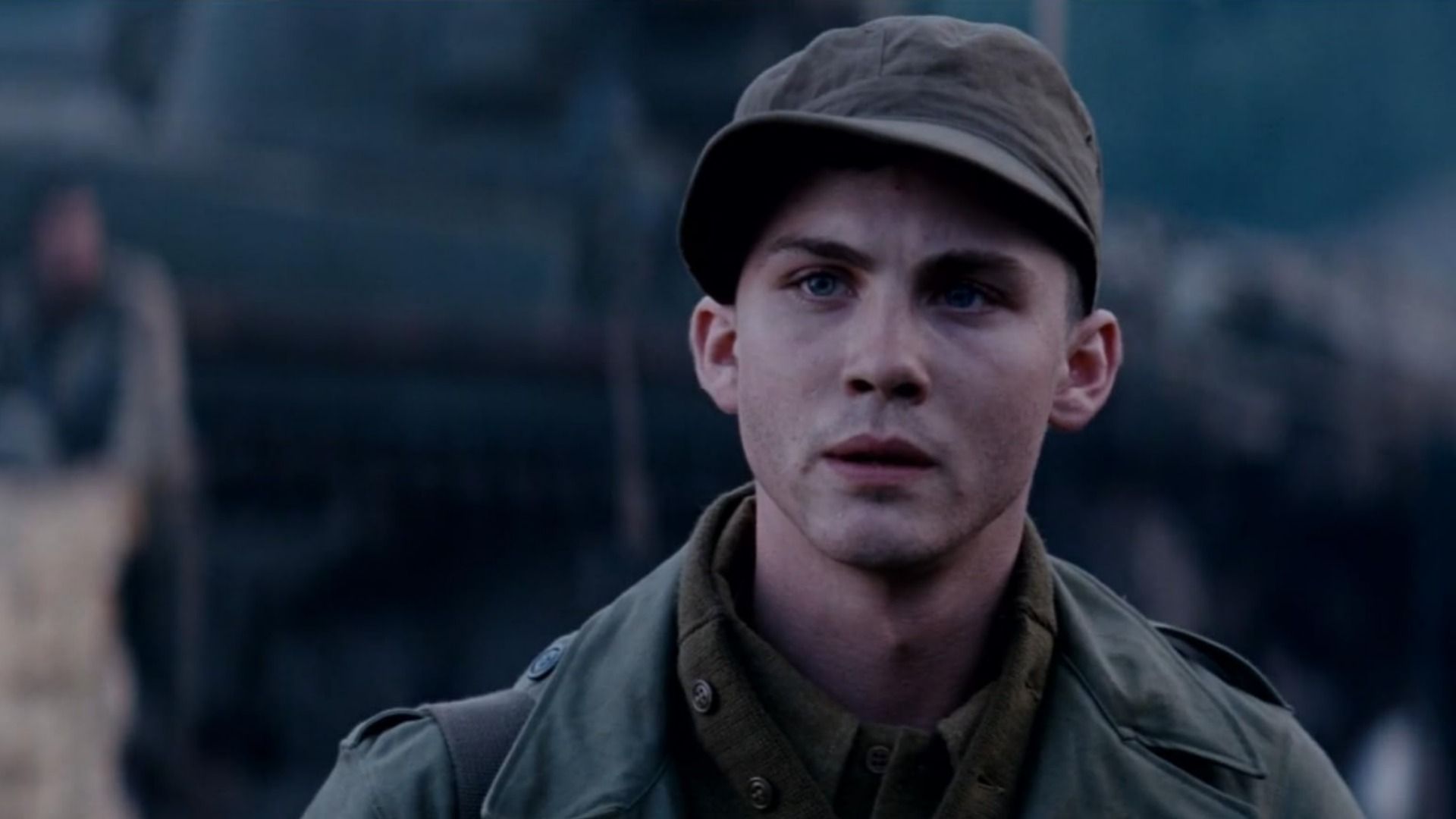 Ator Logan Lerman em uniforme militar com um boné na cabeça