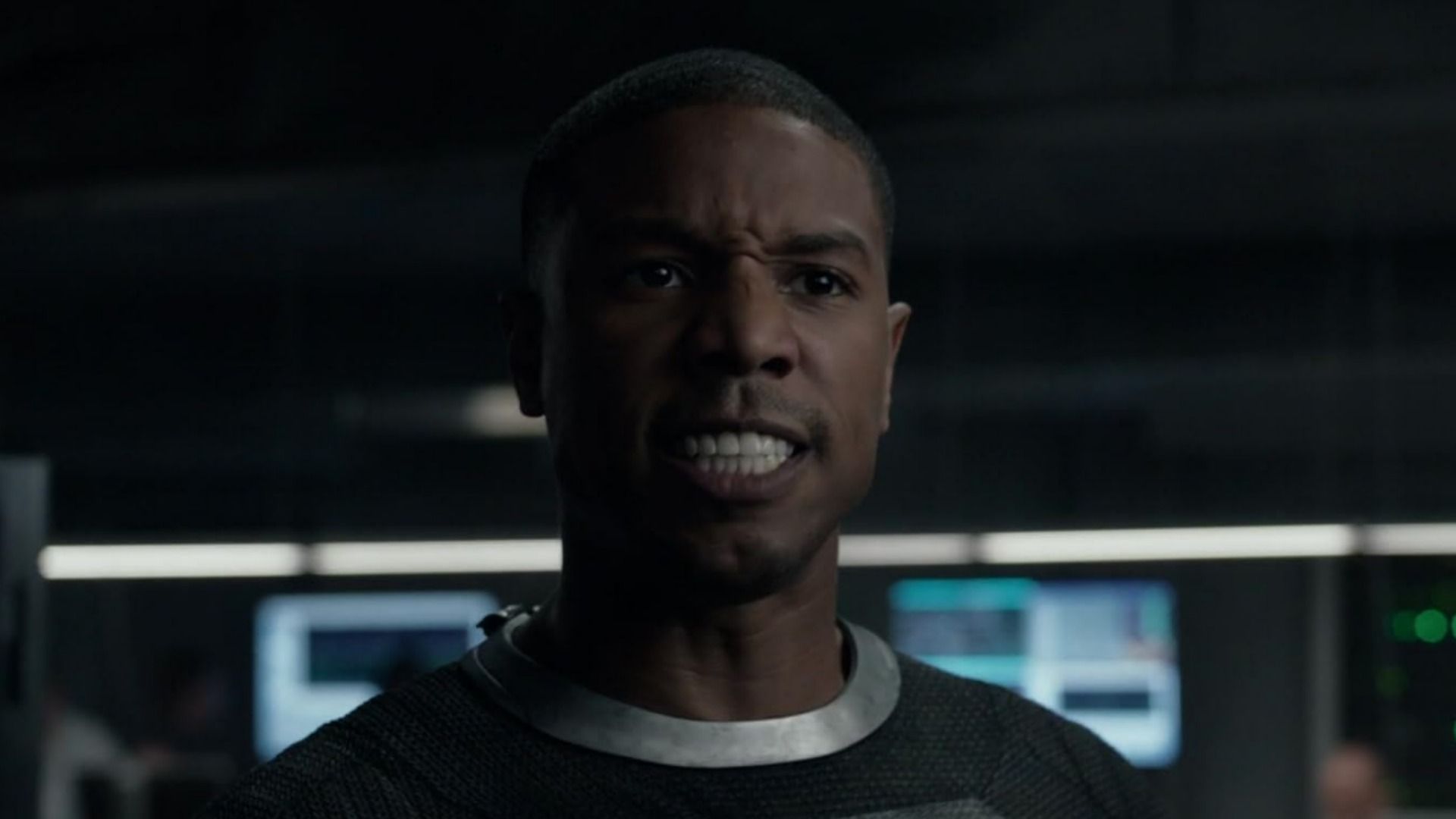 Ator Michael B. Jordan num fato cinzento com ar zangado contra um fundo desfocado