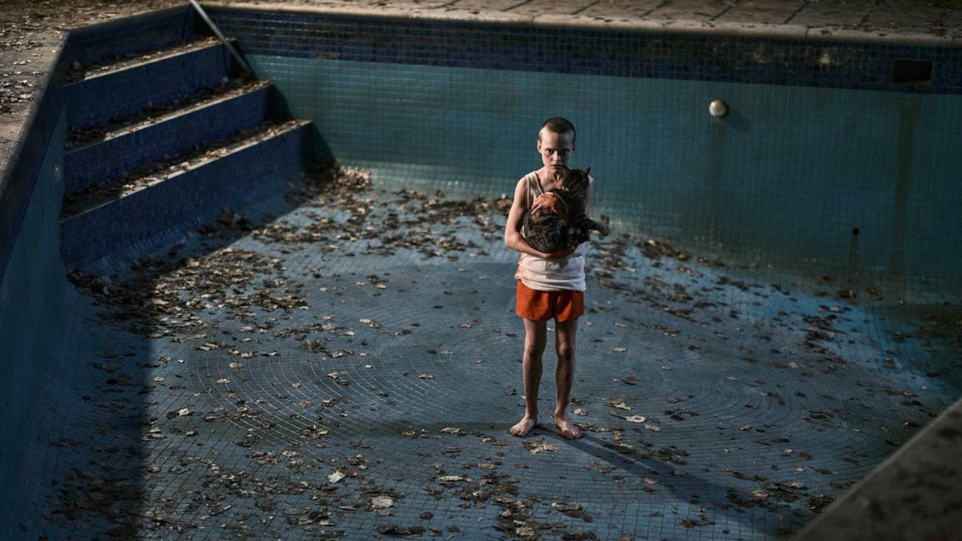 Um rapaz de calções laranja está no fundo de uma piscina segurando um gato