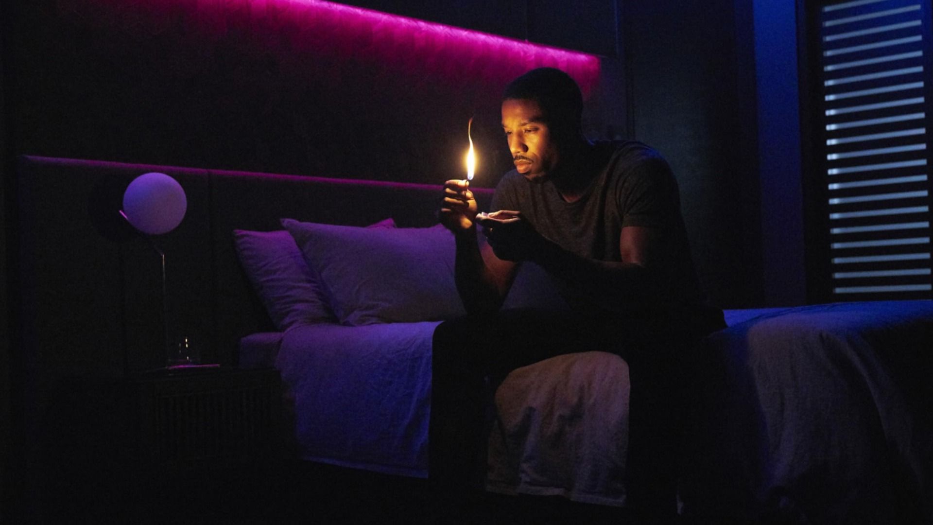 O ator Michael B. Jordan está sentado numa cama com um fósforo nas mãos