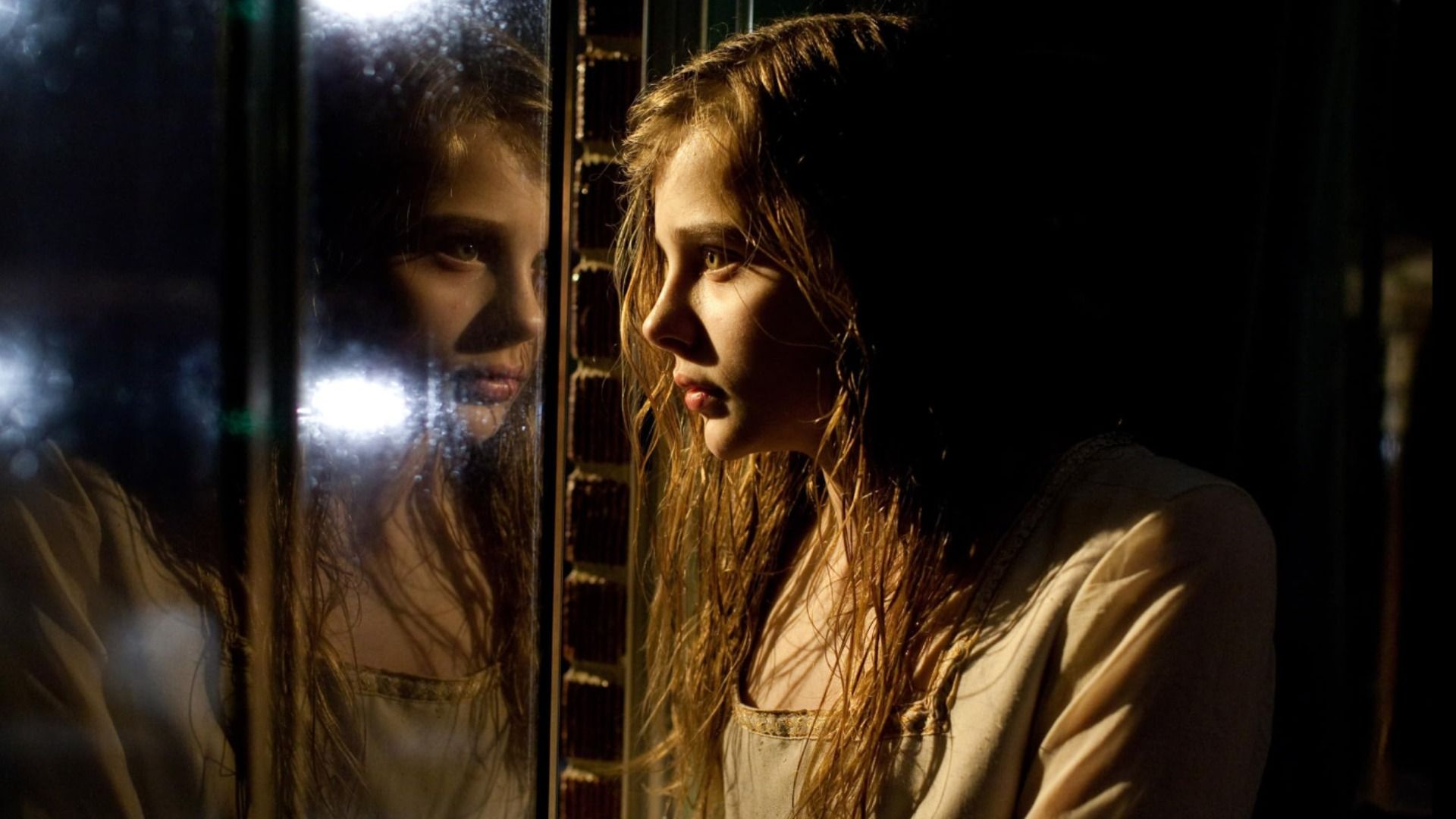 A atriz Chloë Grace Moretz olha para o seu reflexo na janela