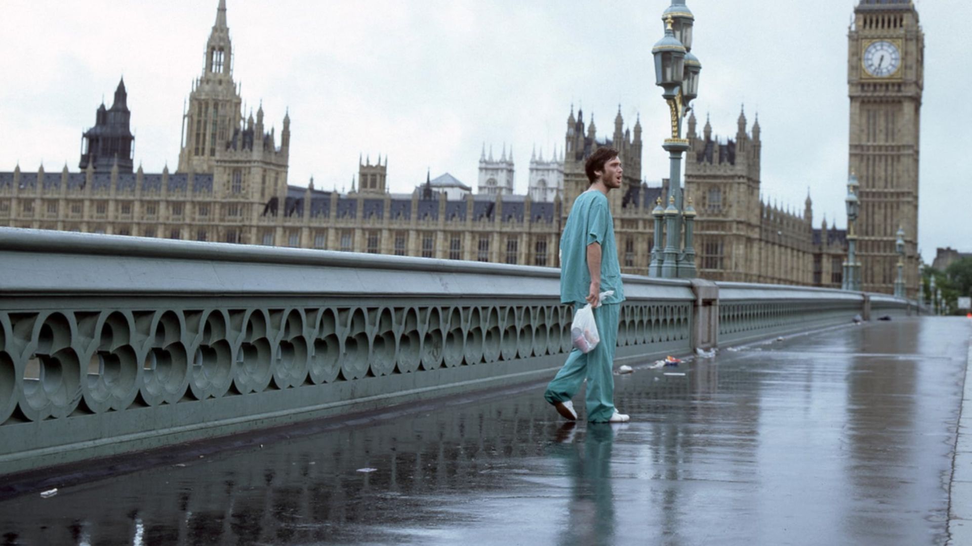 O ator Cillian Murphy com roupa azul está numa ponte vazia com a torre do relógio Big Ben de Londres visível nas proximidades