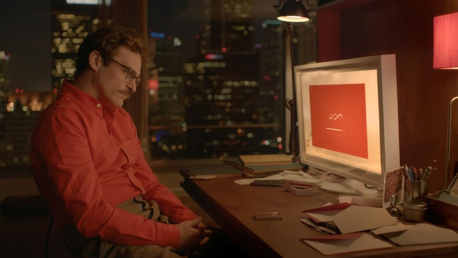 O ator Joaquin Phoenix numa camisa vermelha sentado numa mesa com um computador