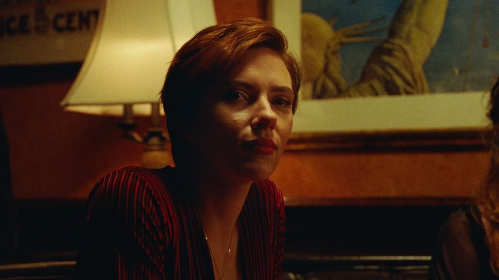 A atriz Scarlett Johansson numa blusa vermelha sentada ao lado de uma lâmpada